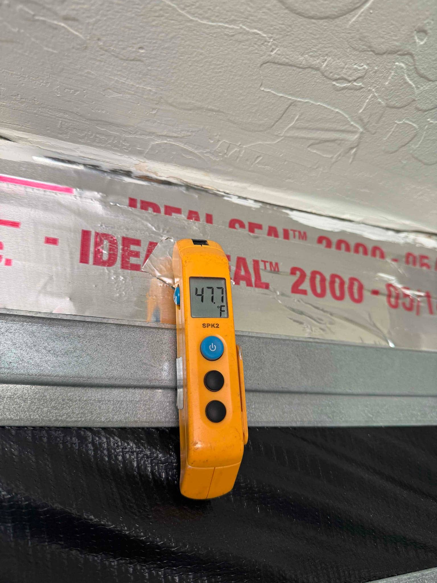 Digital thermometer displays 47.7 °F while measuring the surface temperature of an insulated HVAC duct.