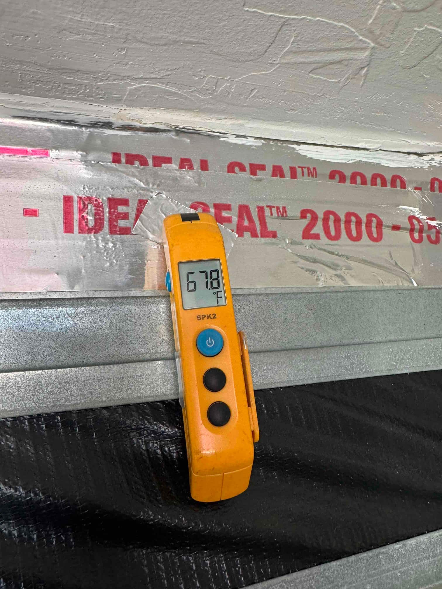 Digital thermometer displays 67.8 °F while measuring air temperature adjacent to a sealed HVAC duct with foil tape.