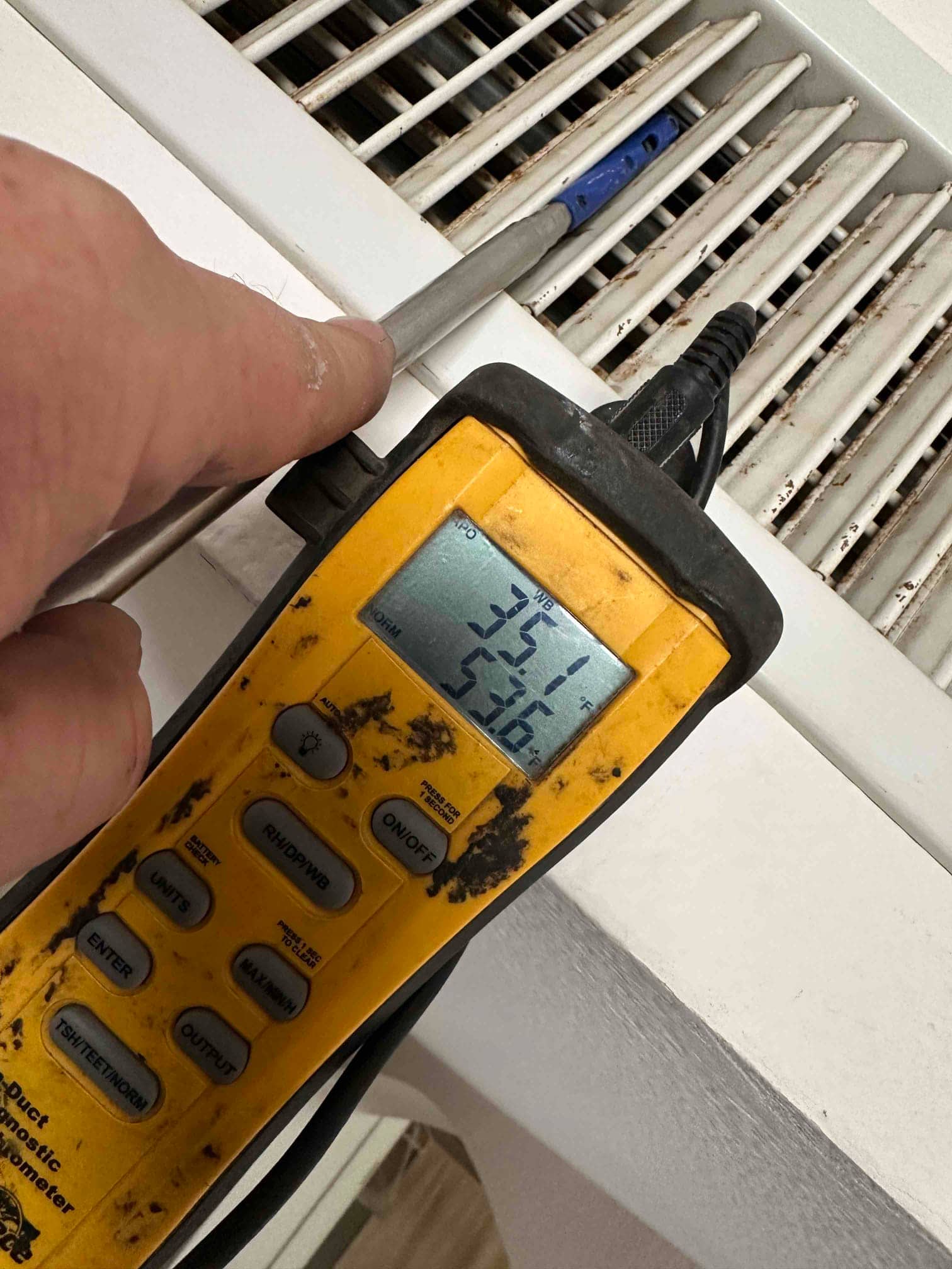 Digital thermometer probe inserted into a supply register shows cooled air temperature readings on the handheld display.