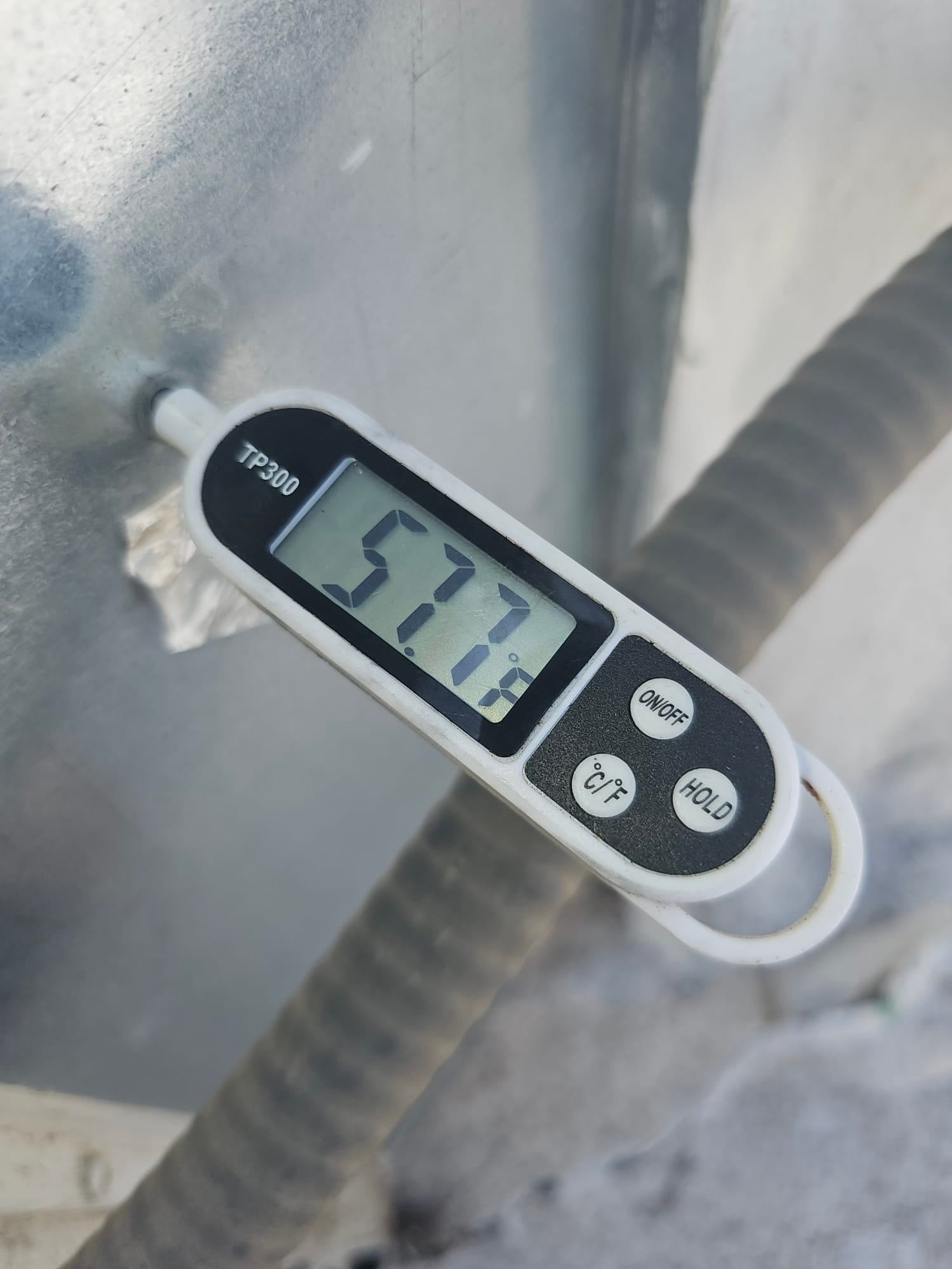 Digital thermometer probe measures 57.7 °F at a metal surface next to flexible conduit.