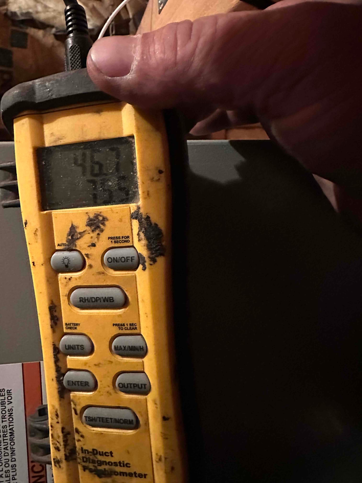 Digital thermometer probe measures supply air temperature at the air handler, display reading 46.7 degrees Fahrenheit during cooling operation.