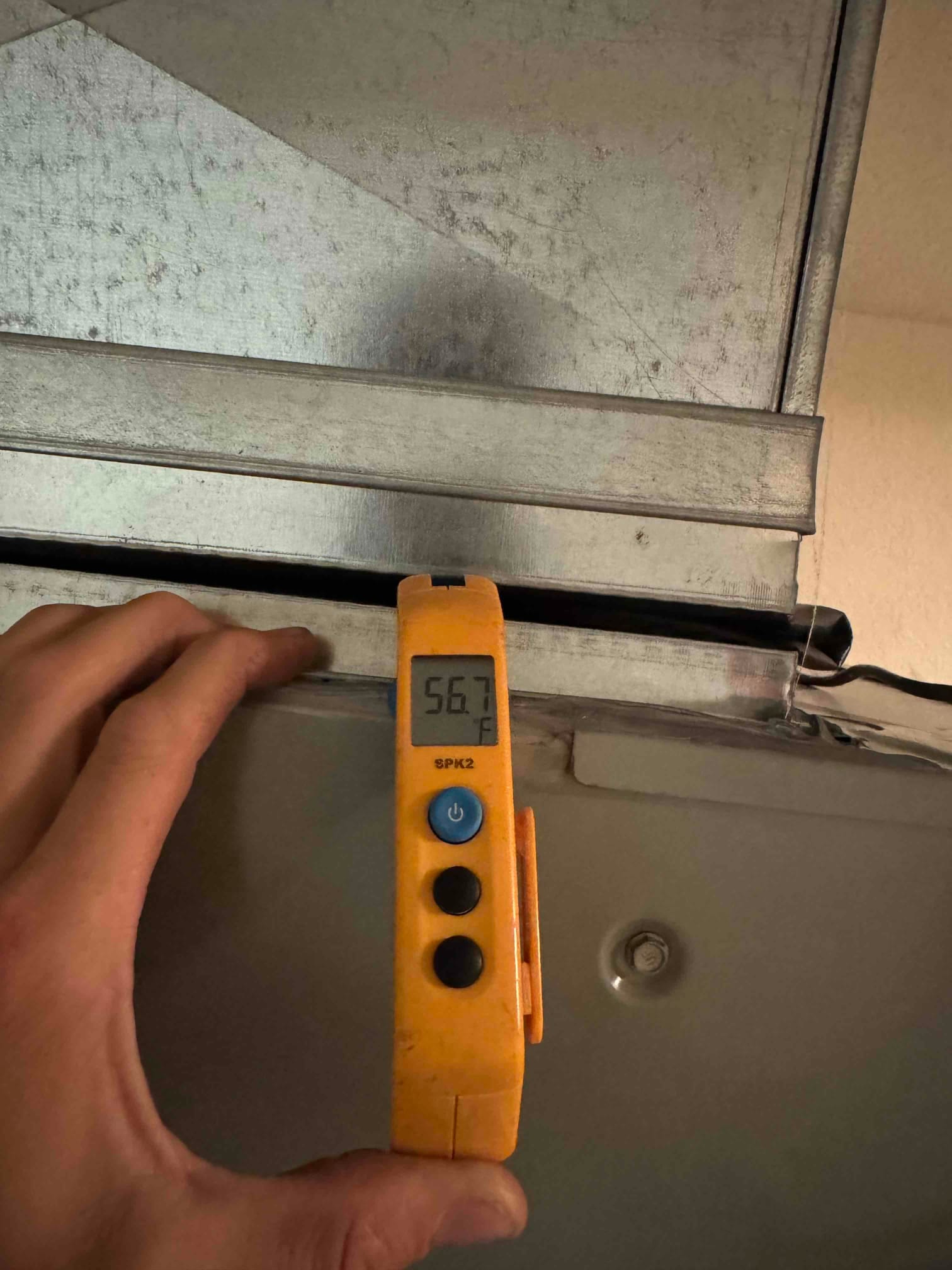 Digital thermometer shows 56.7 °F supply air temperature at a metal duct, probe clipped to the duct surface.