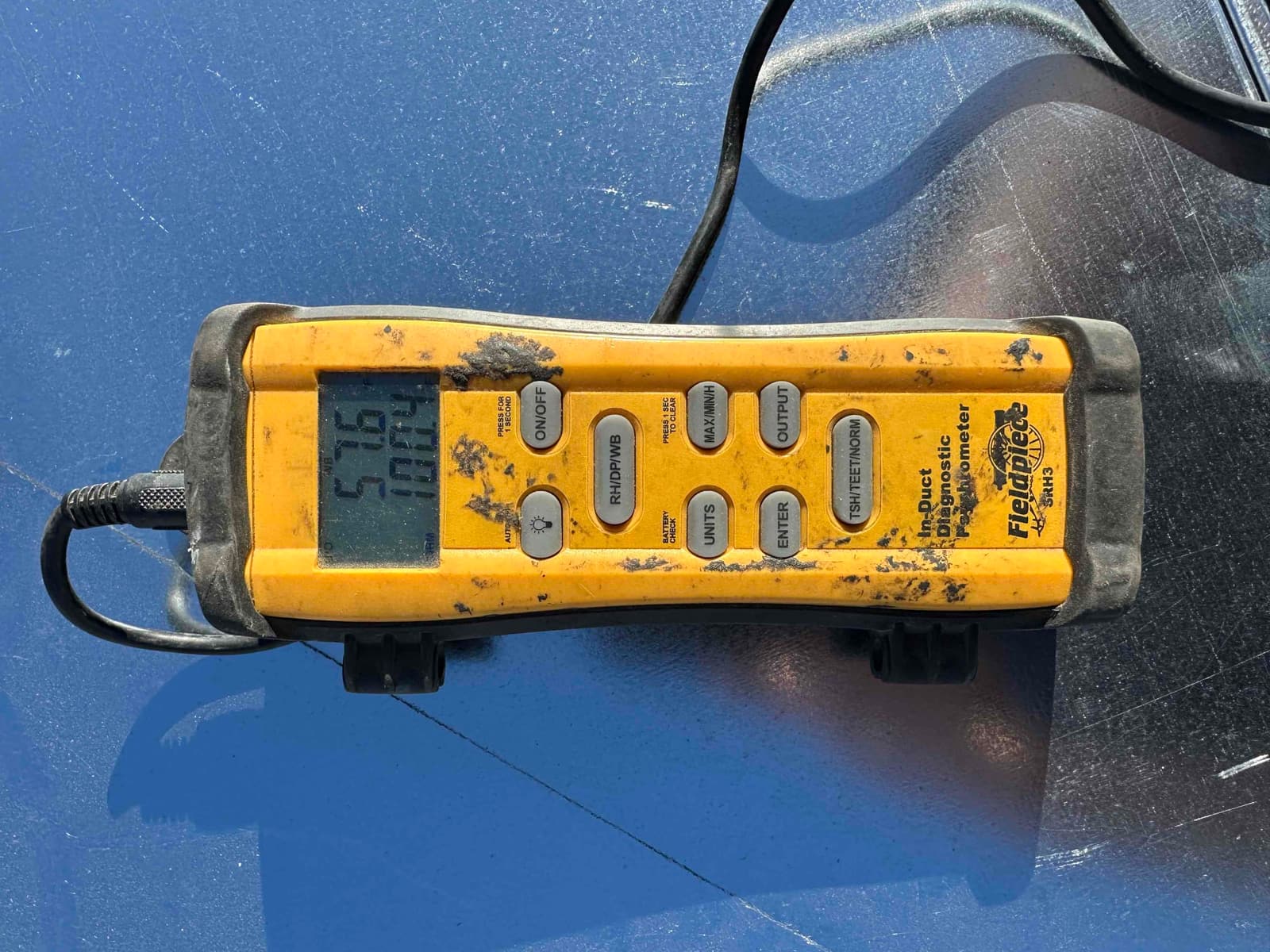 Digital thermometer shows 57.6°F during supply air measurement to document cooling performance at the duct.