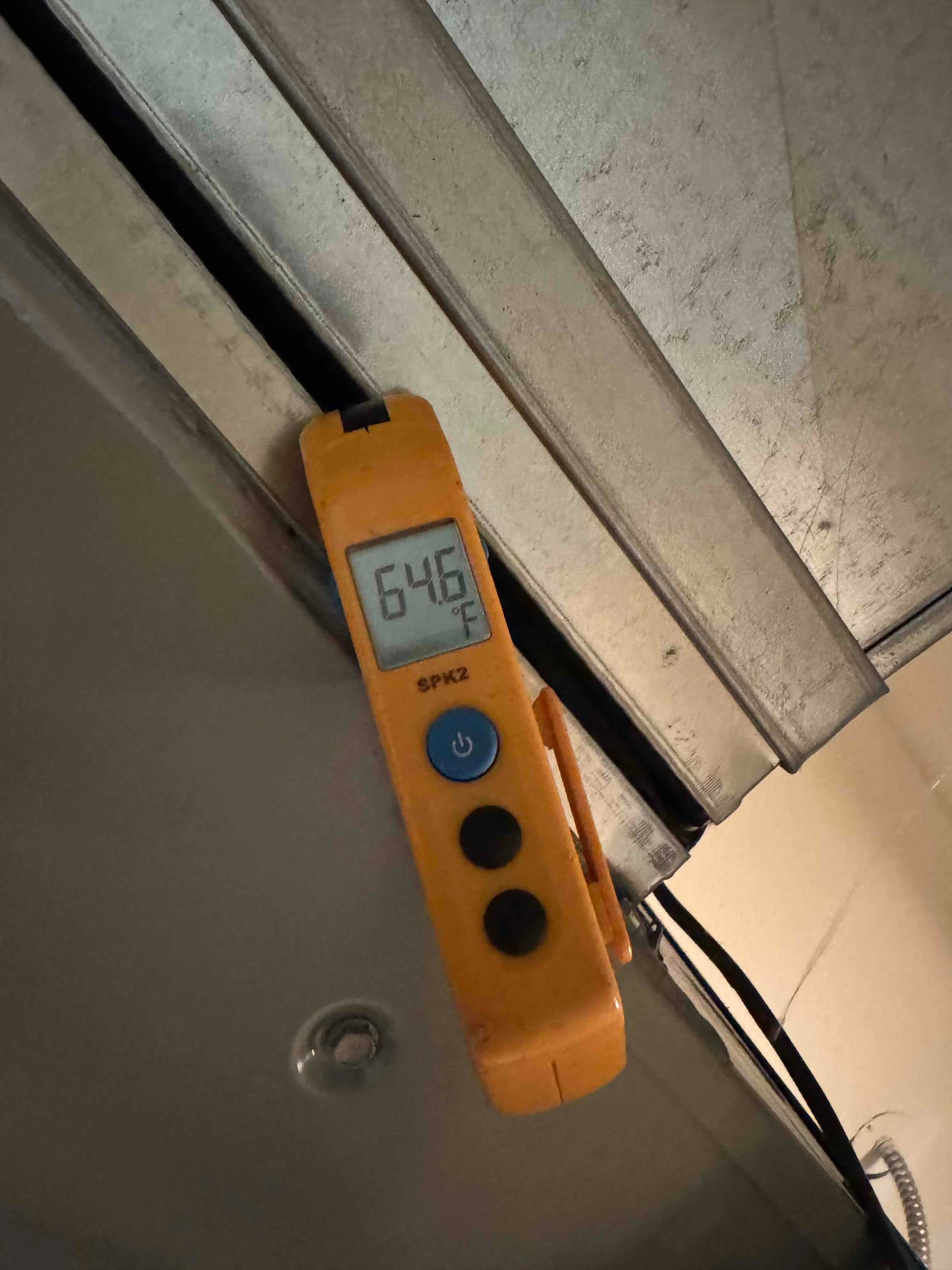 Digital thermometer shows 64.6 °F at the duct edge inside the HVAC system.