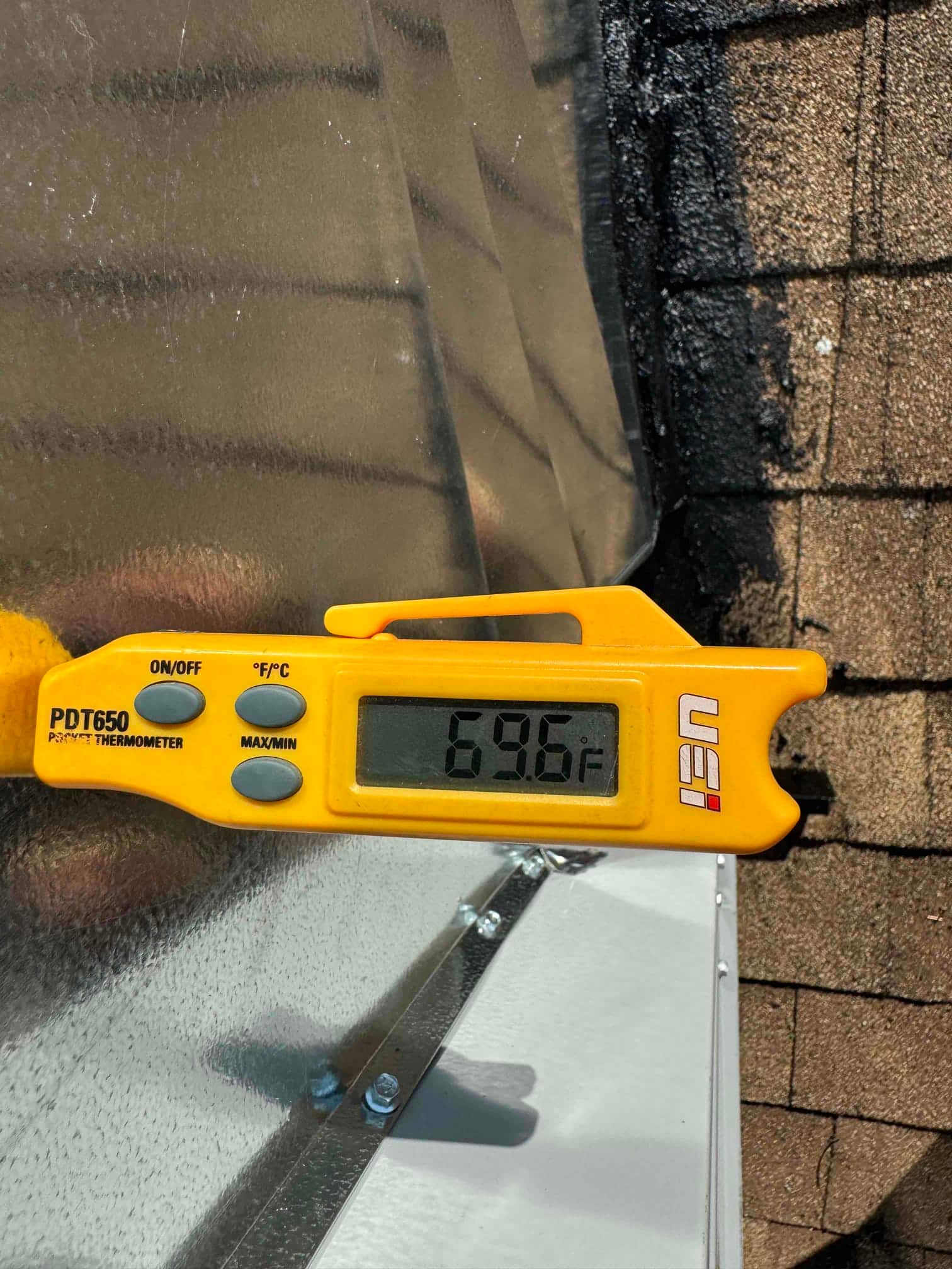 Digital thermometer shows 69.6°F while measuring air temperature near newly installed metal duct connection on the rooftop unit.