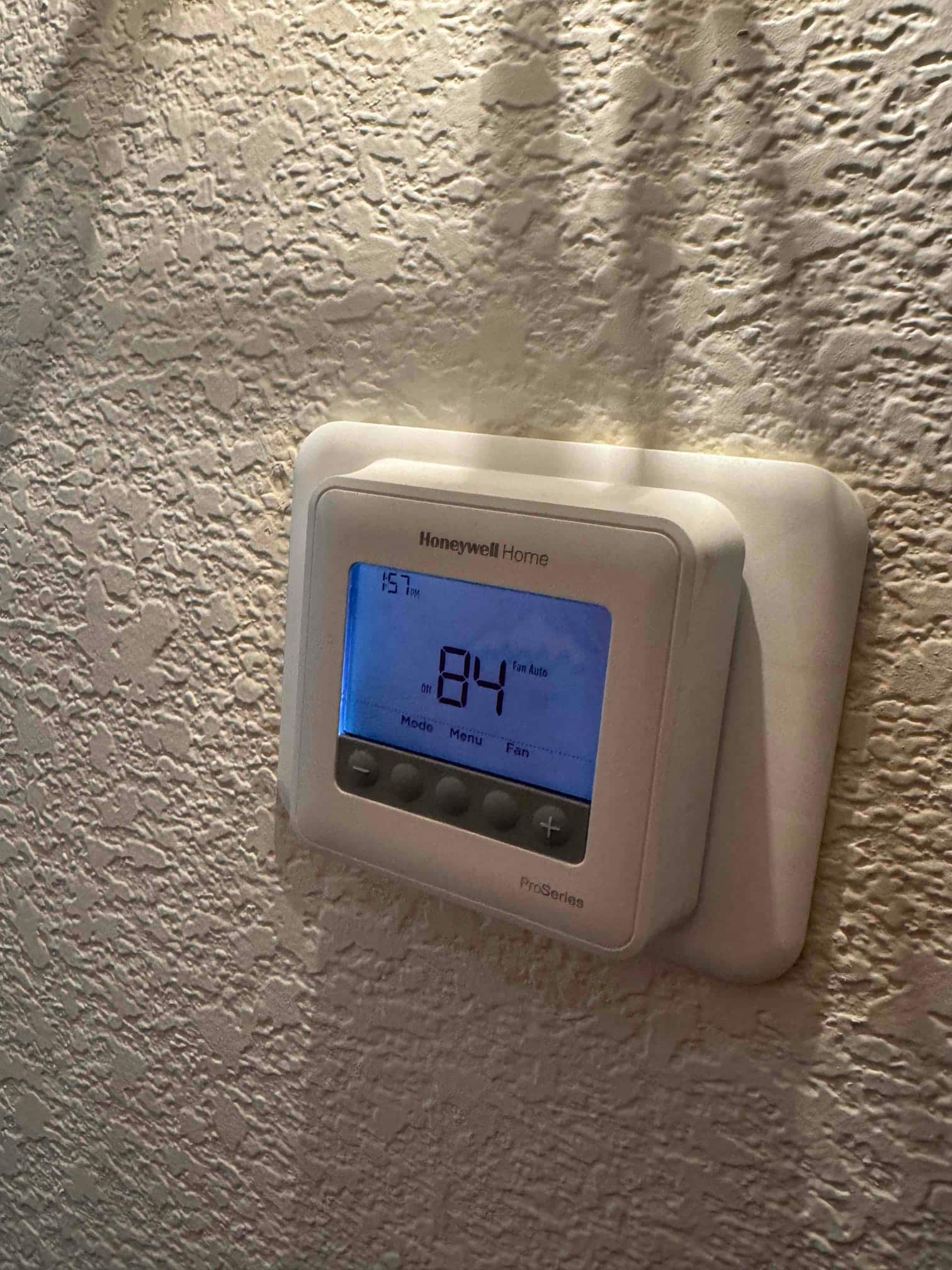 Digital thermostat on textured wall displays 84°F indoor temperature with fan and mode buttons visible.