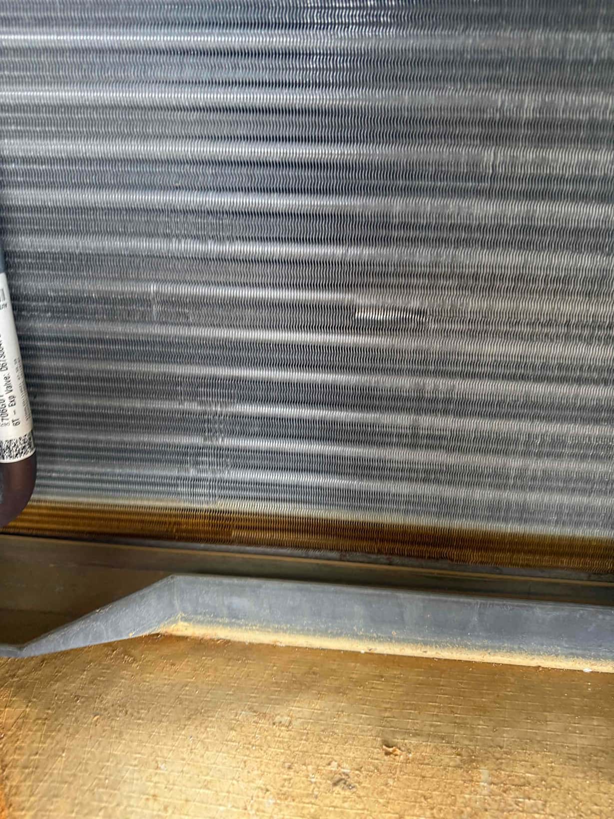 Evaporator coil fins and drain pan interior, showing clean fin surfaces and accumulated condensate staining along the pan edge.