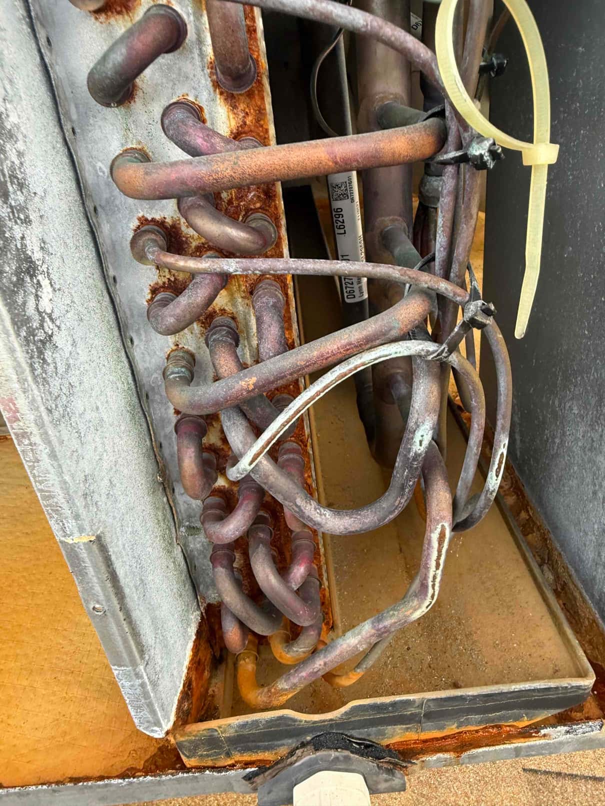 Evaporator coil section with heavily rusted copper tubing and corroded metal housing, showing deterioration and oxidation on multiple bends.