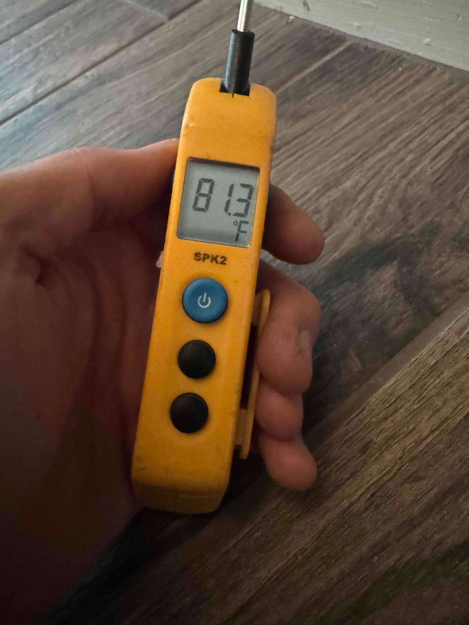 Handheld digital thermometer displays 81.3 °C on the probe-connected screen during HVAC temperature measurement.