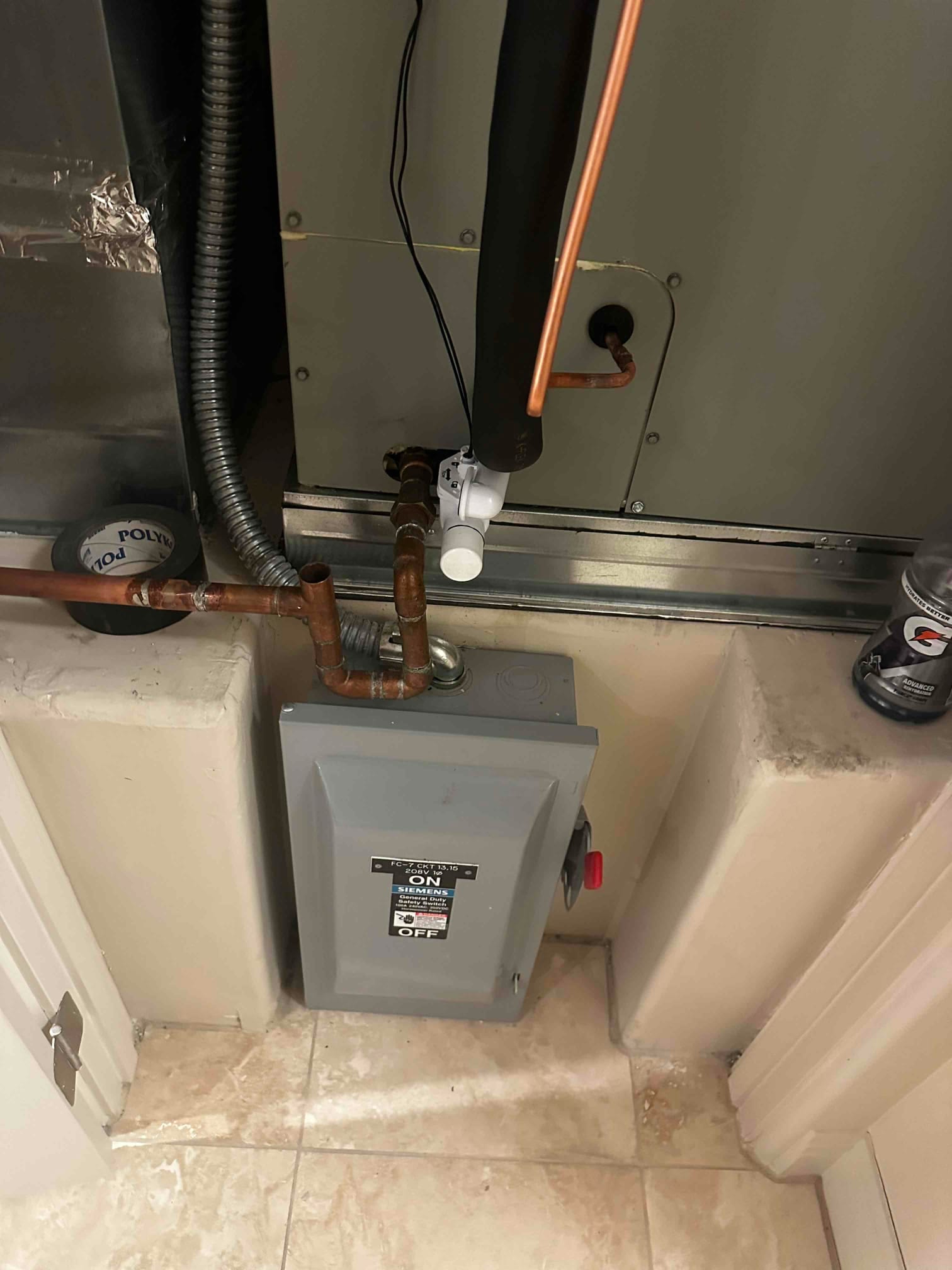 Indoor air handler installation with insulated suction line, copper refrigerant lines, condensate safety switch, and mounted disconnect box.
