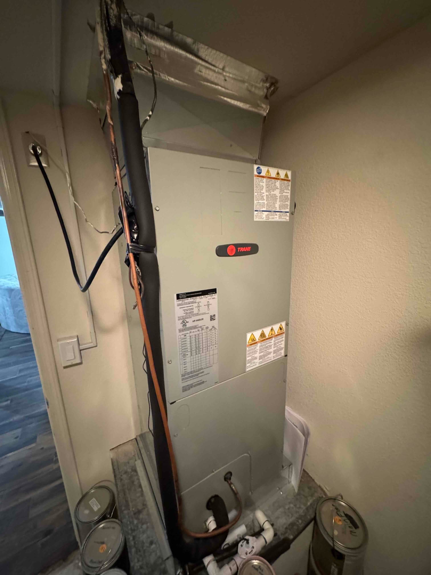 Indoor air handler with insulated refrigerant lines, condensate drain, and electrical wiring visible in a closet installation.