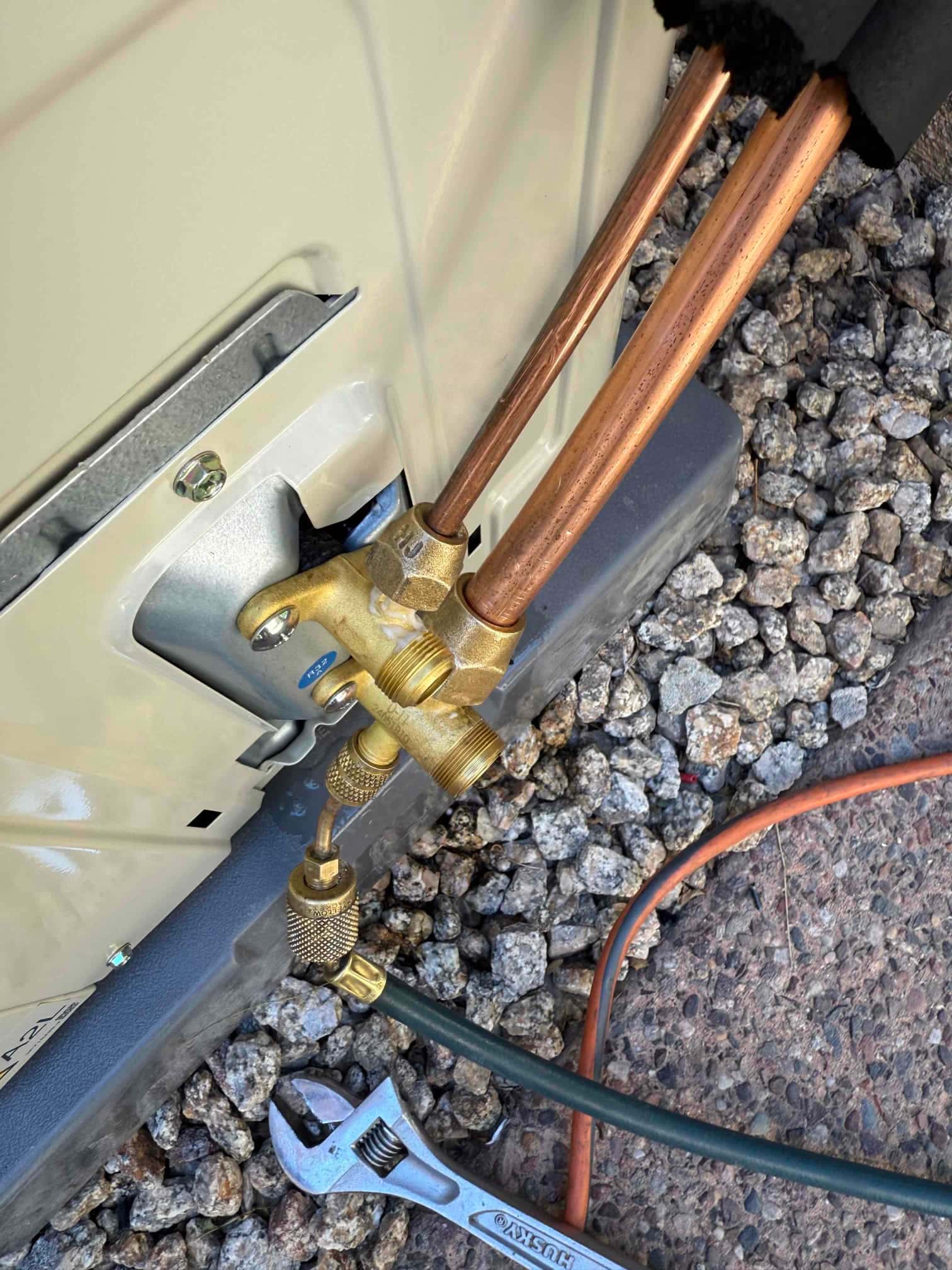 Mini-split service valves with connected hose and insulated copper line set at the outdoor unit during installation.