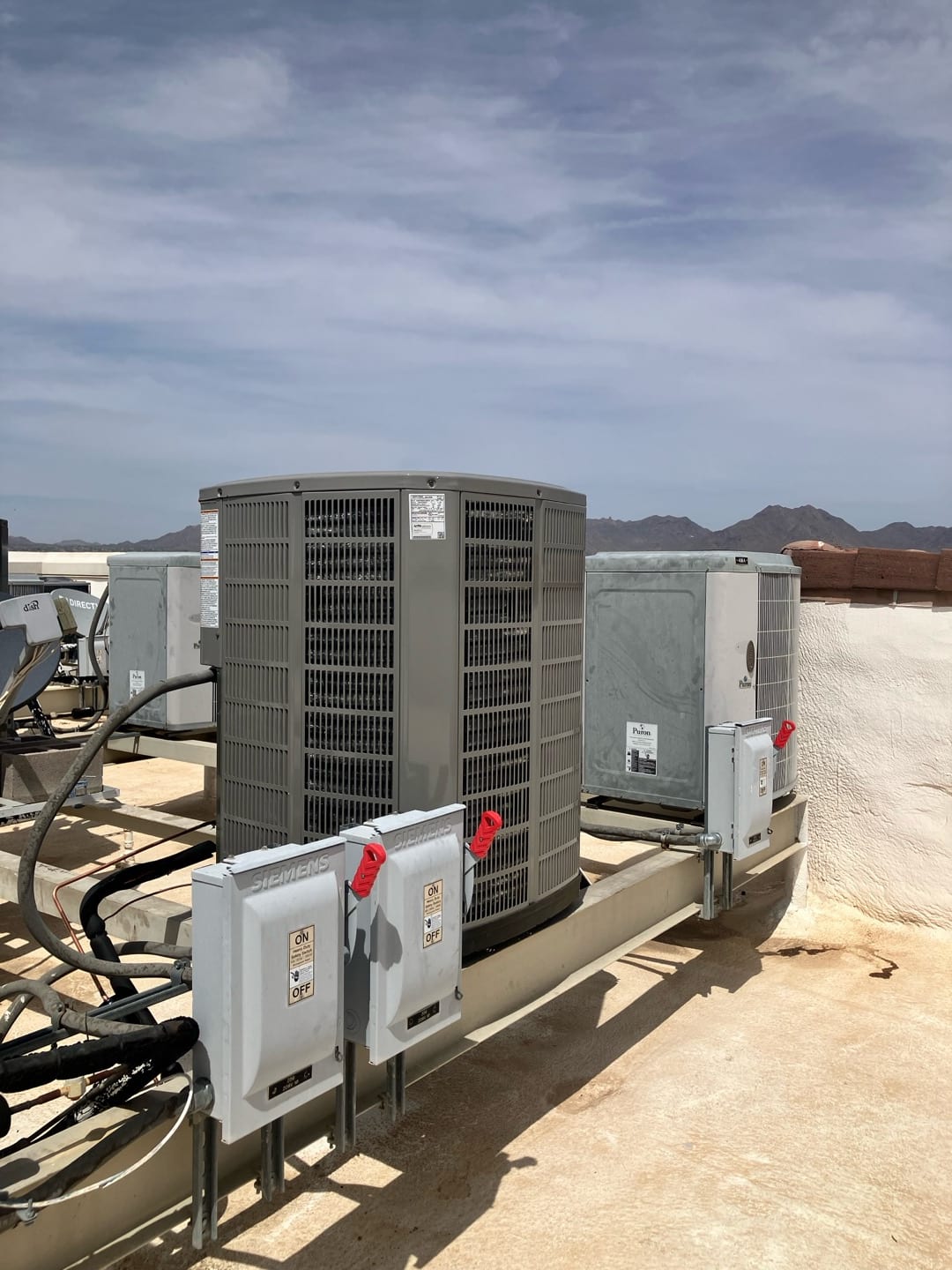 Multiple rooftop condensers set on a metal equipment stand with mounted service disconnects and insulated refrigerant line sets.