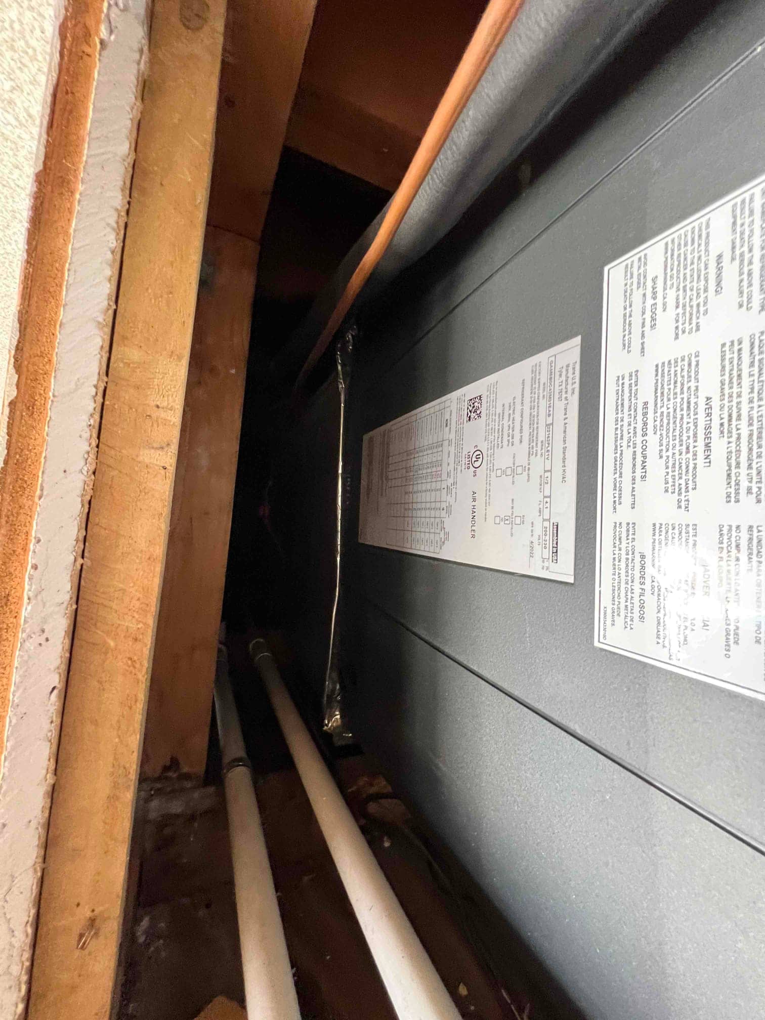 New air handler installed in attic bay with insulated refrigerant line and PVC condensate drains routed along the joists.