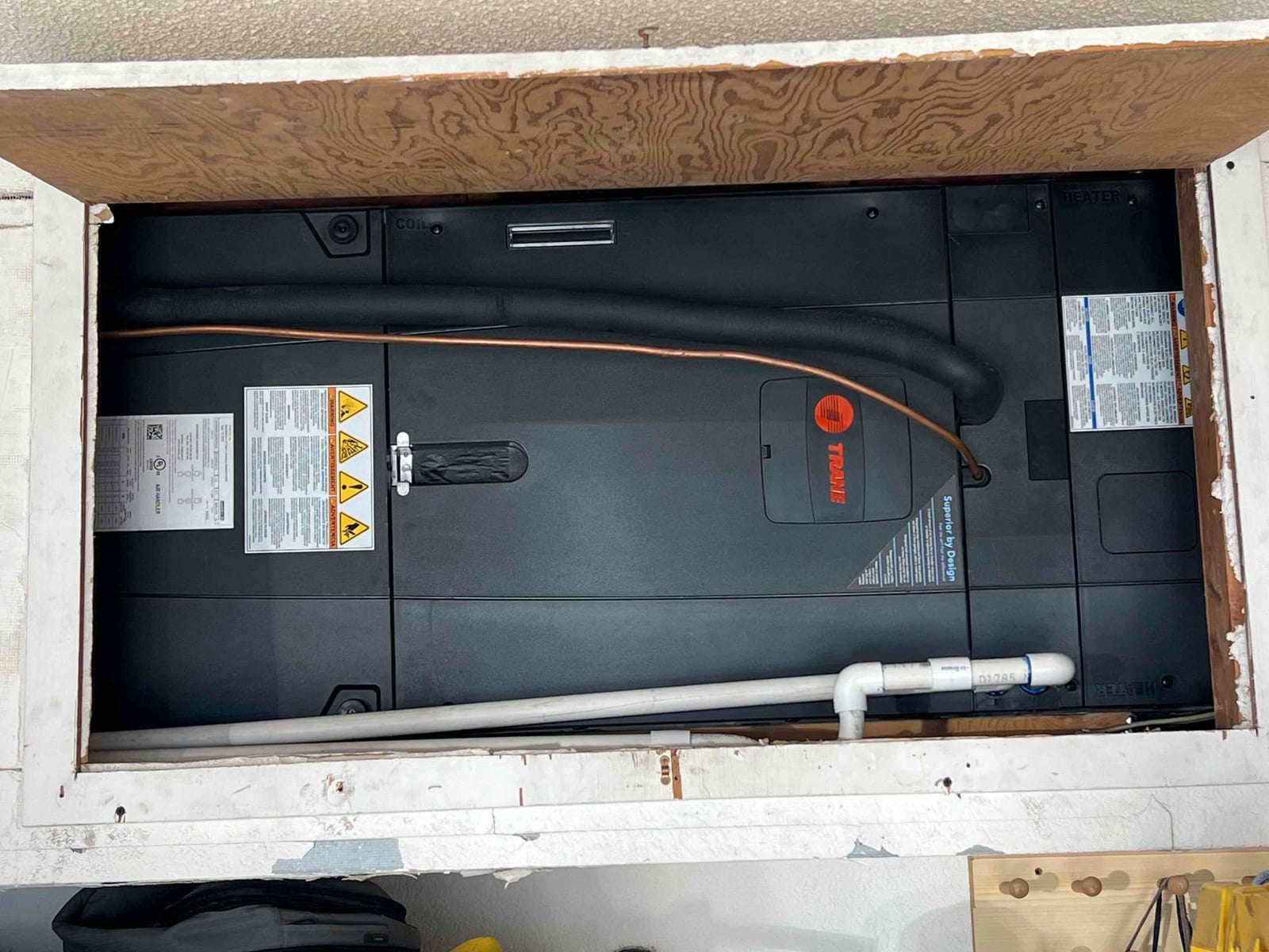New horizontal air handler set in a ceiling platform with insulated refrigerant lines and PVC condensate drain piping connected.