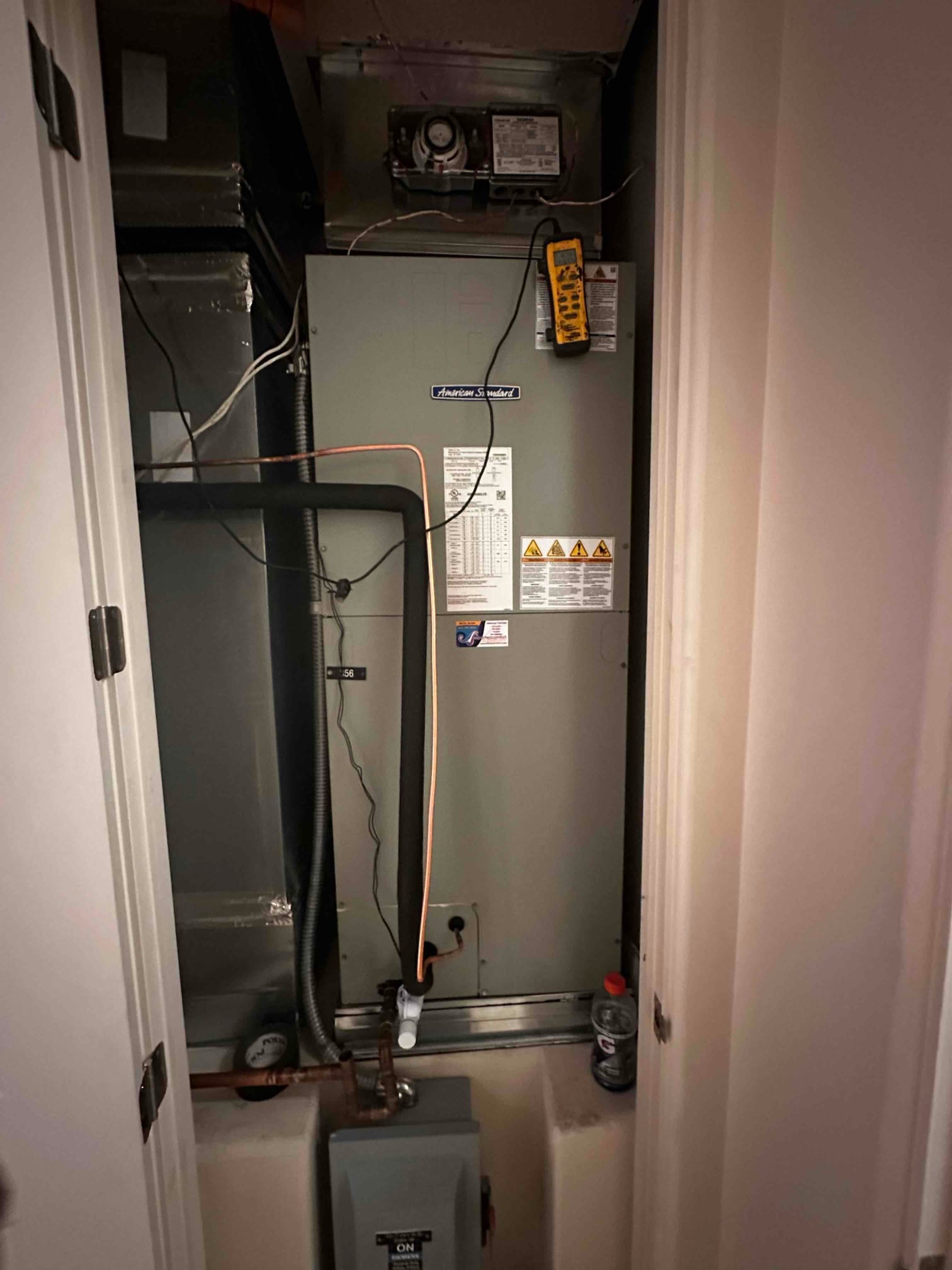 New indoor air handler installed in closet with insulated refrigerant lines, condensate drain, duct connections, and service disconnect accessible.