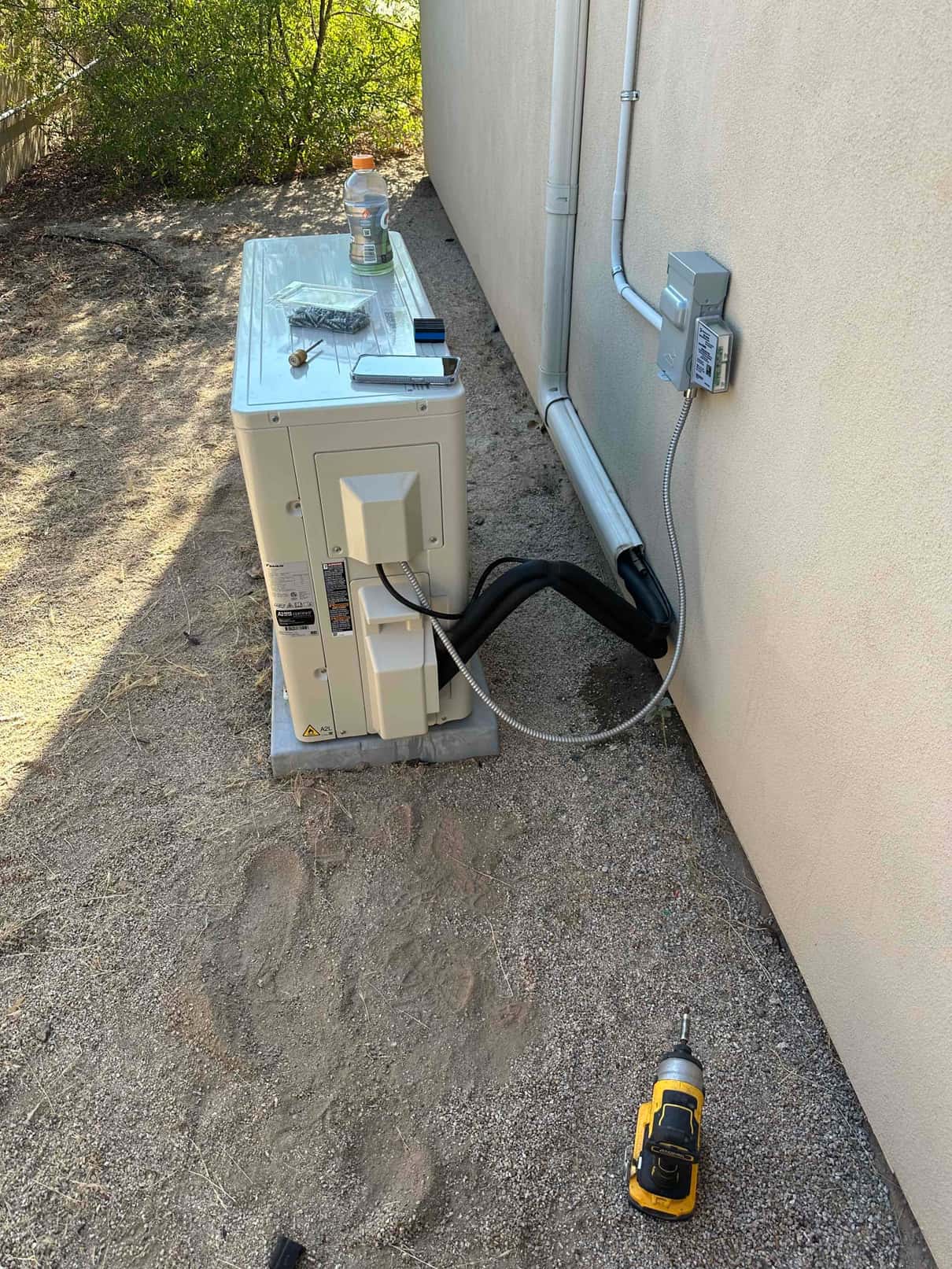 New mini-split outdoor unit set on a pad with sealed line set cover and mounted electrical disconnect conduit.