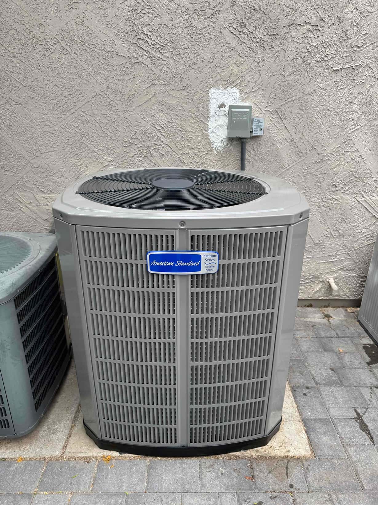 New outdoor condenser set on a level pad with nearby electrical disconnect mounted on the wall and sealed penetration.