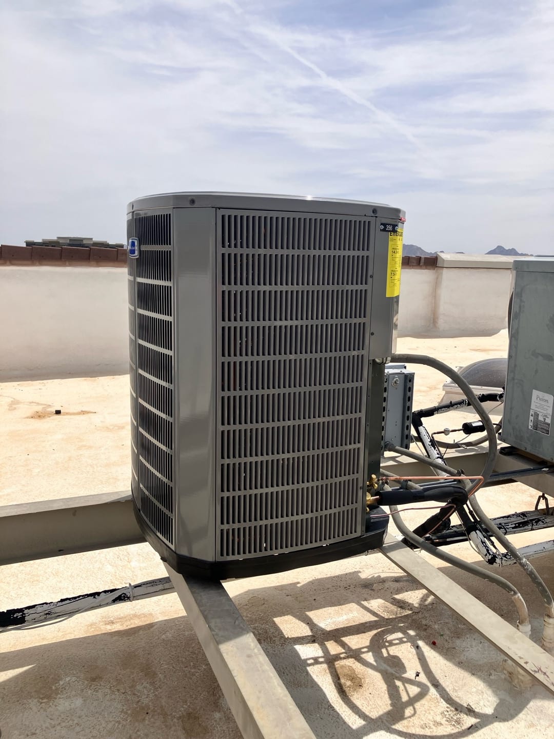 New outdoor heat pump condenser set on a rooftop support frame with connected refrigerant lines and electrical whip.
