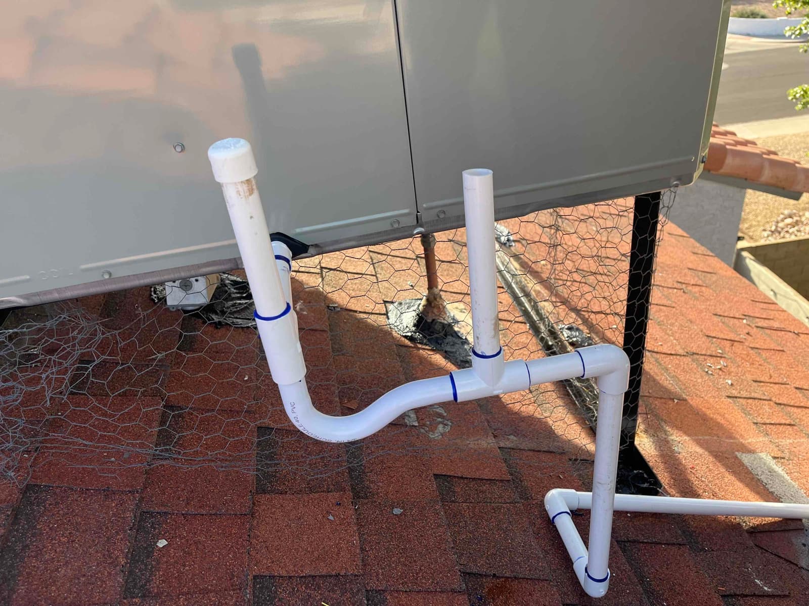 New rooftop condensate drain assembly with primary and secondary PVC standpipes connected to the packaged unit, sealed at the roof penetration.