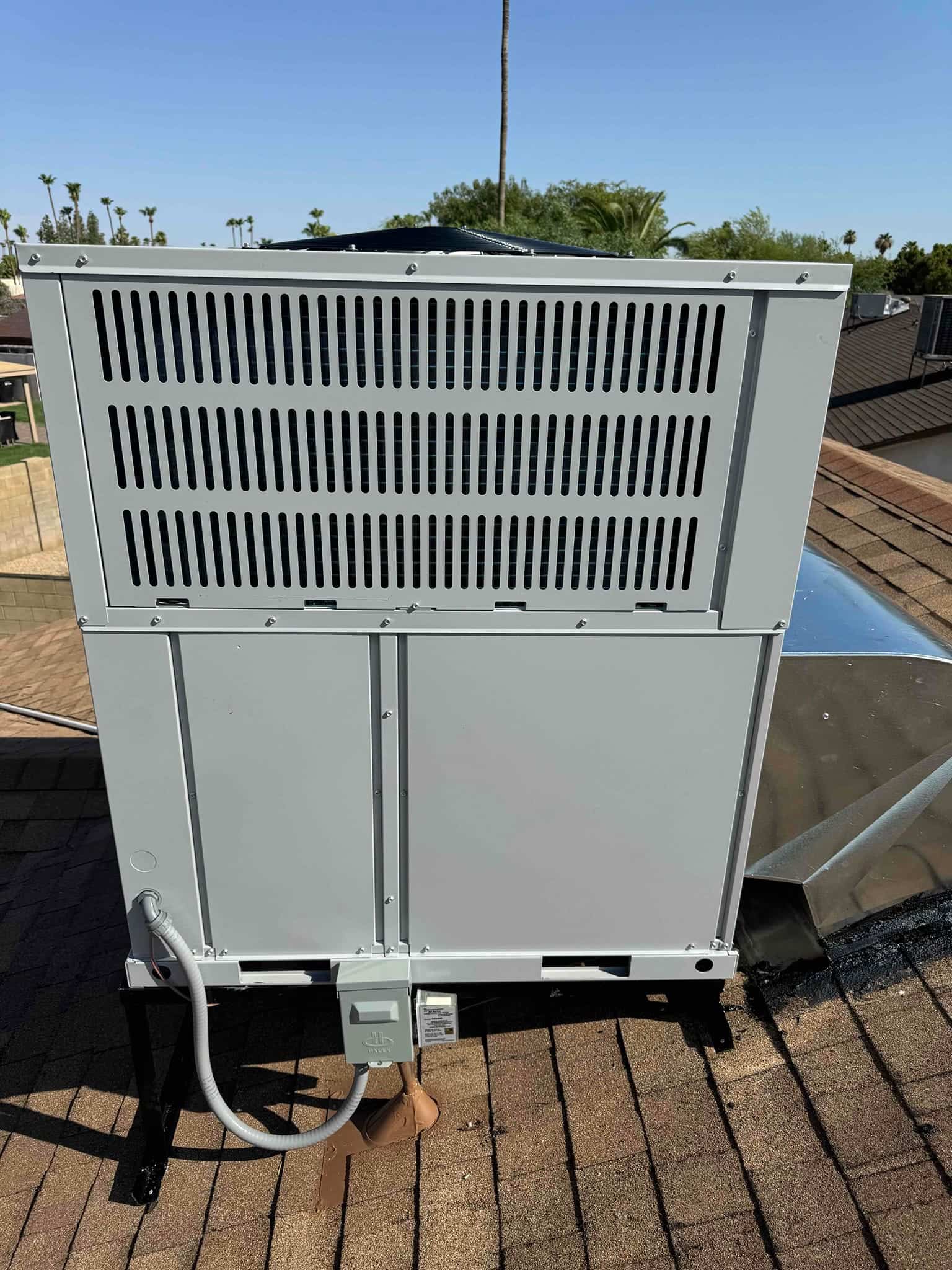 New rooftop heat pump condenser set on a metal stand with weatherproof disconnect and flexible whip installed.