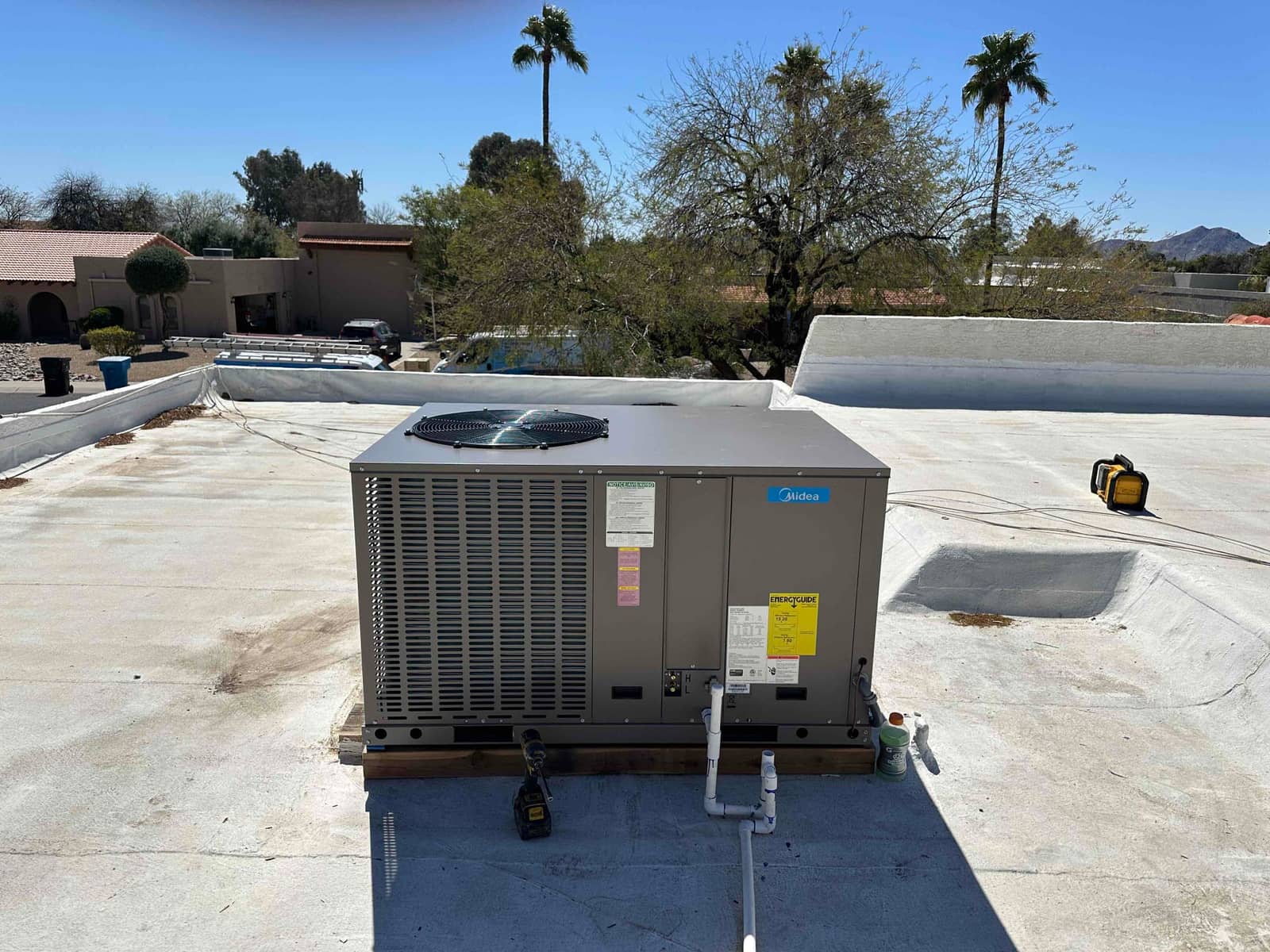 New rooftop package HVAC unit installed on curb with connected condensate drain and sealed roof penetration, tools staged nearby.
