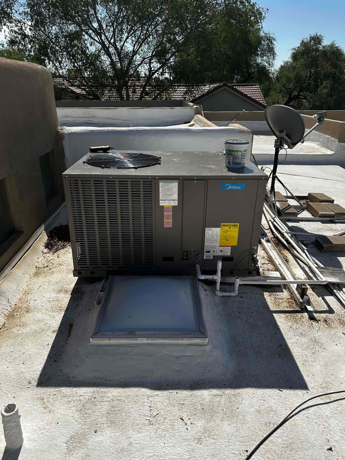 New rooftop package HVAC unit set on a coated flat roof with drain piping connected and sealed roof penetration nearby.