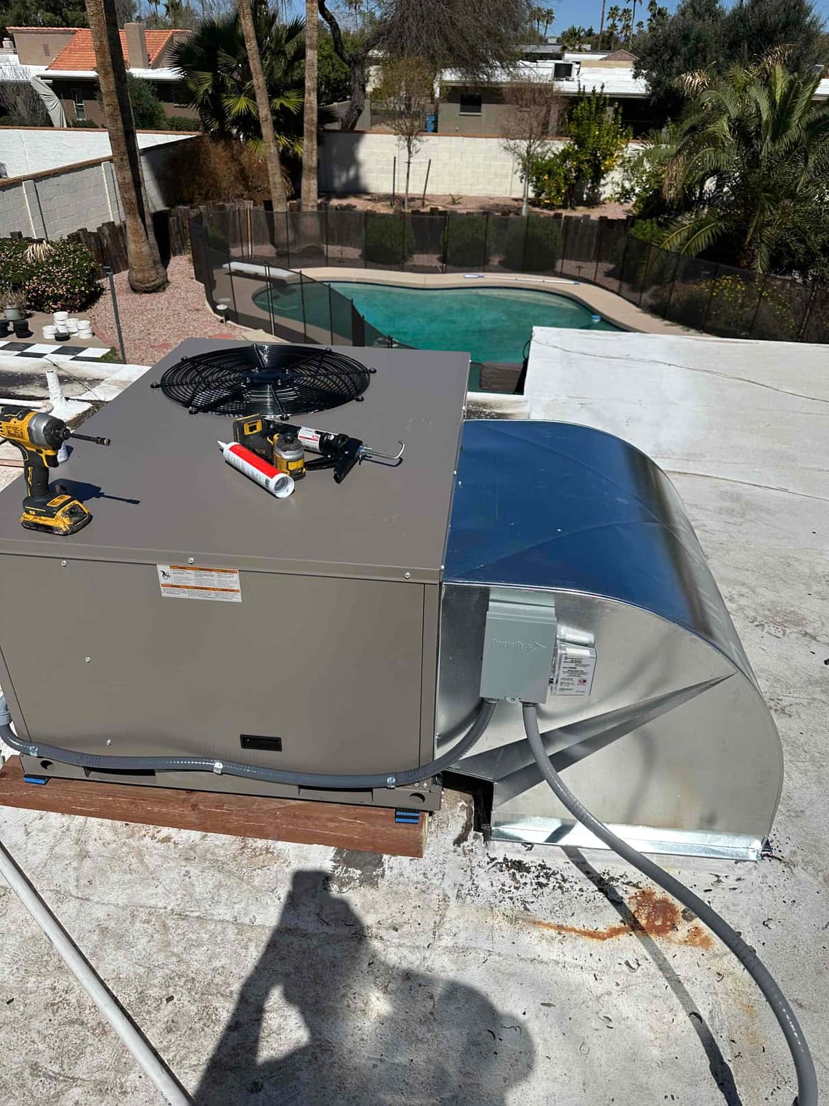 New rooftop packaged HVAC unit installed on curb with sealed duct transition, electrical disconnect, and tools on top during setup.