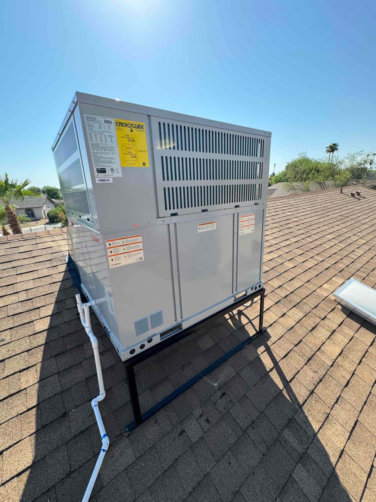 New rooftop packaged HVAC unit installed on a steel stand with routed condensate drain piping and sealed roof penetrations.