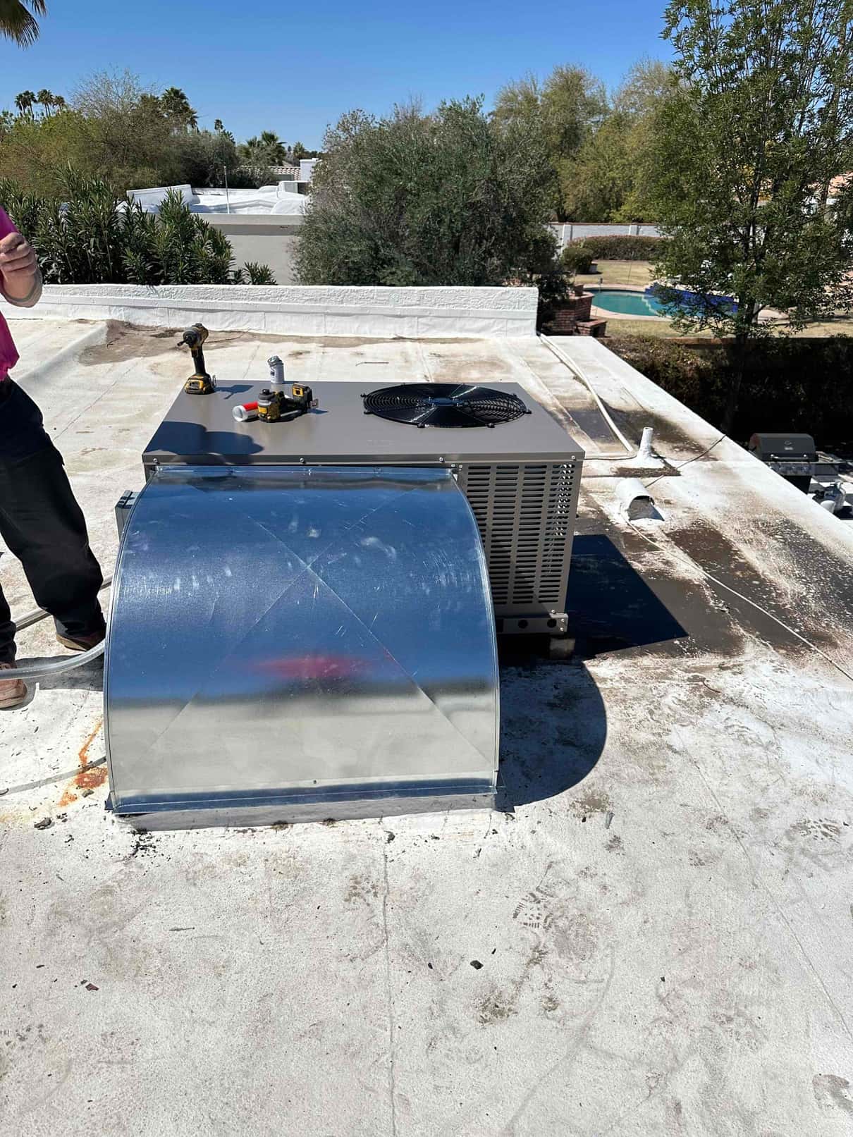 New rooftop packaged HVAC unit set on the roof with a fabricated sheet metal supply plenum and tools on top.