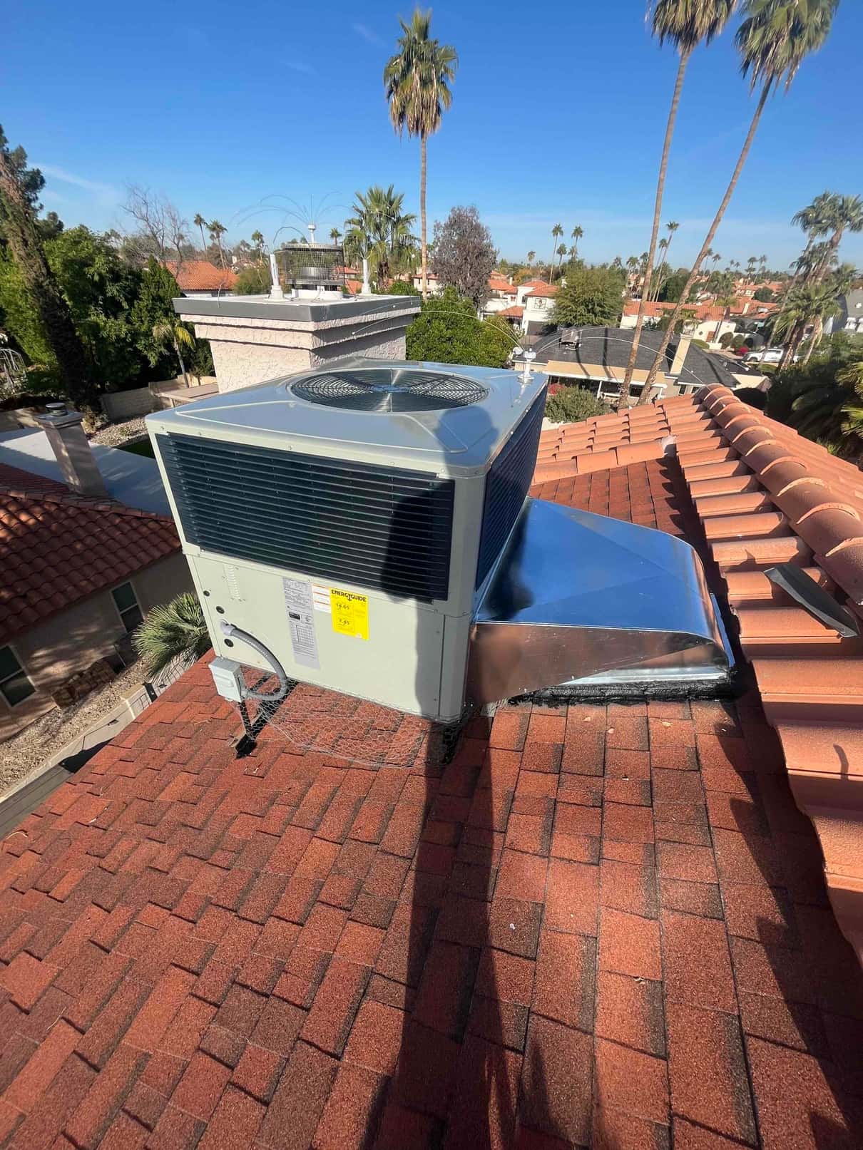New rooftop packaged unit installed on shingles with sealed curb and connected duct transition, shown from above in daylight.