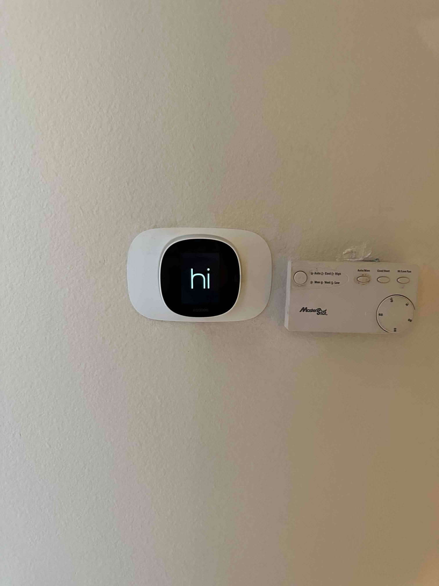 New smart thermostat mounted on the wall next to an older control, completing the HVAC control upgrade.