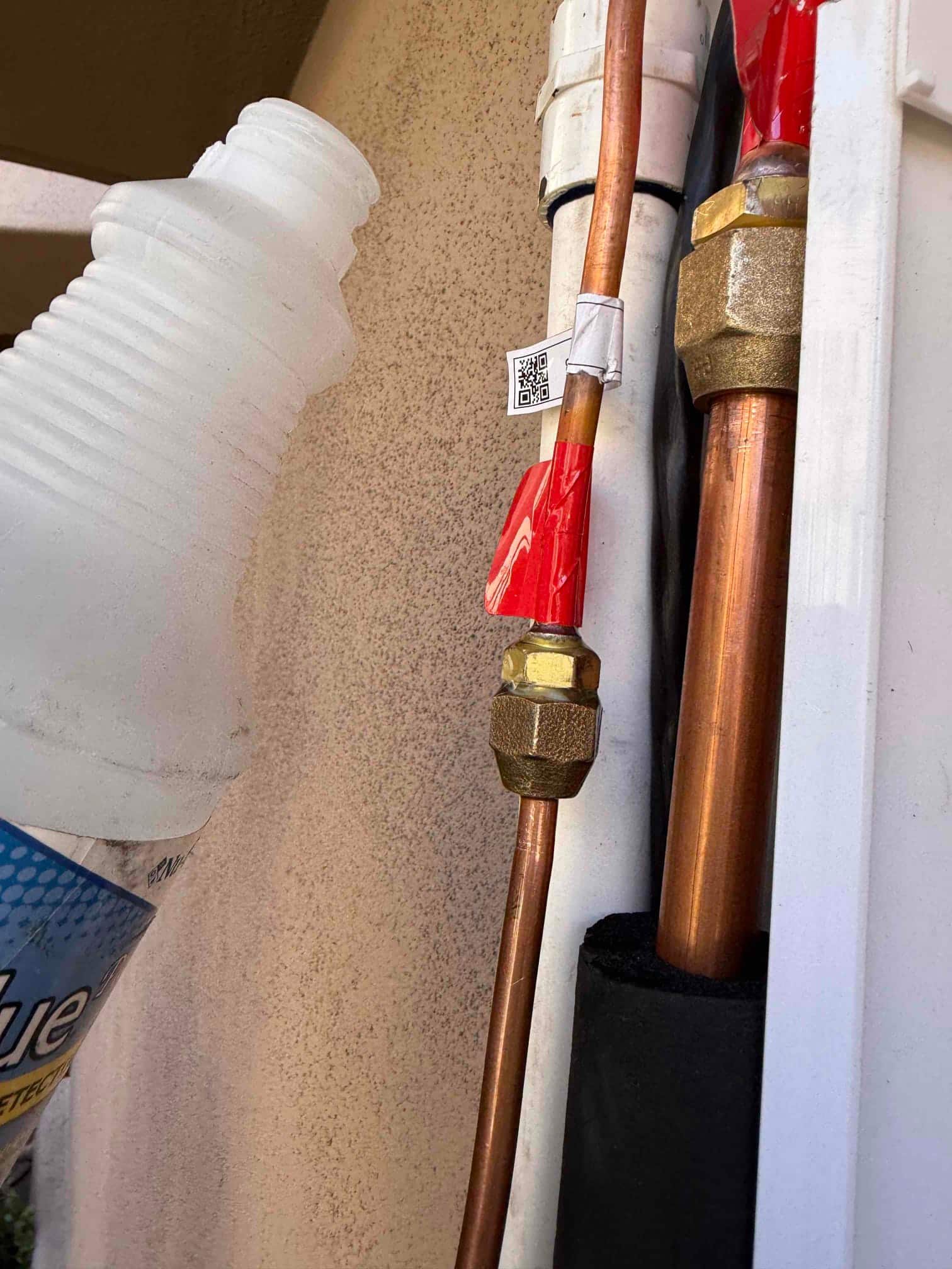 Newly flared and tightened copper refrigerant line connections with red protective caps and insulation at the outdoor mini-split installation.