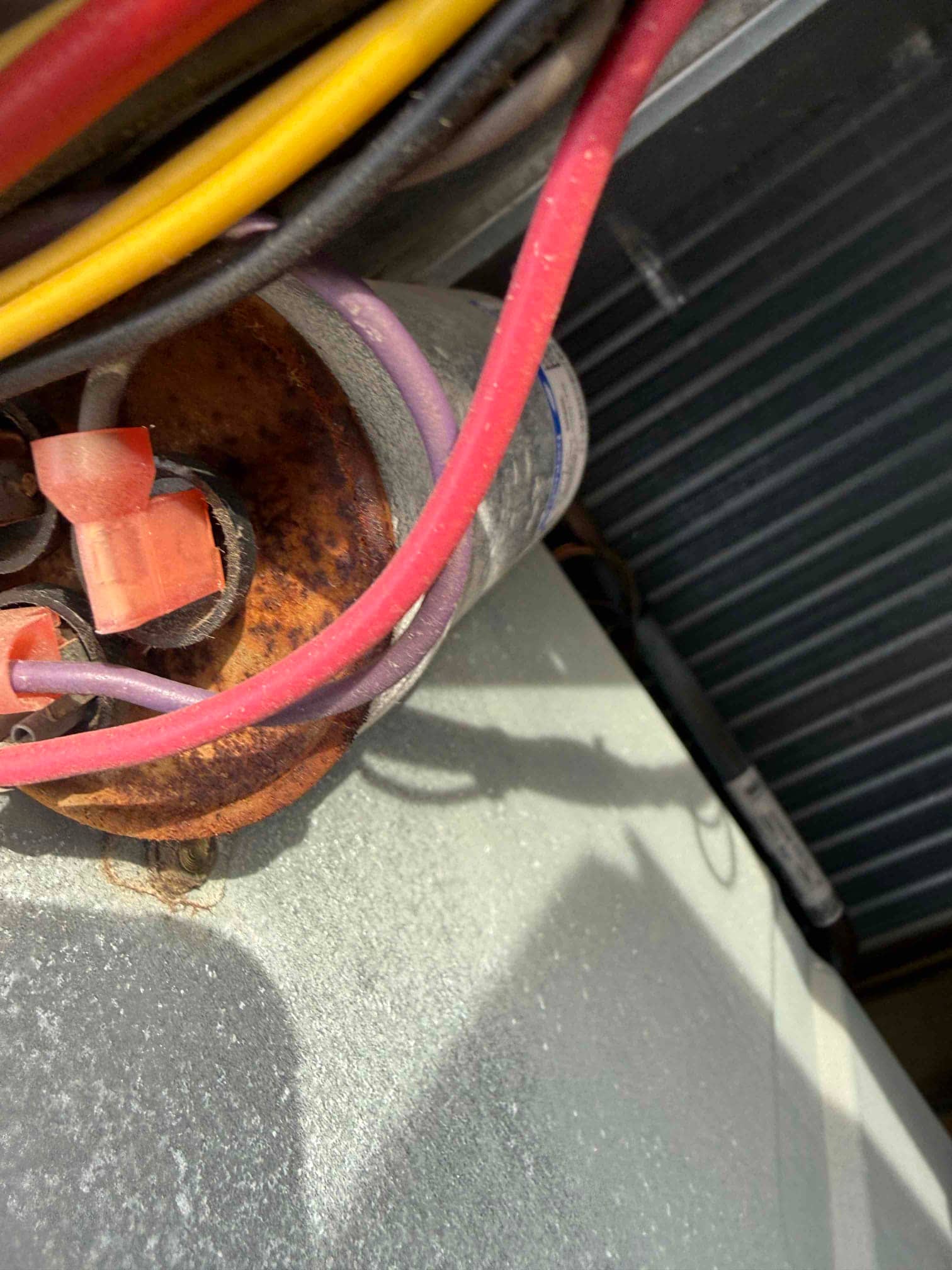 Old rusted capacitor with connected red, yellow, and purple wires inside the outdoor condenser compartment.