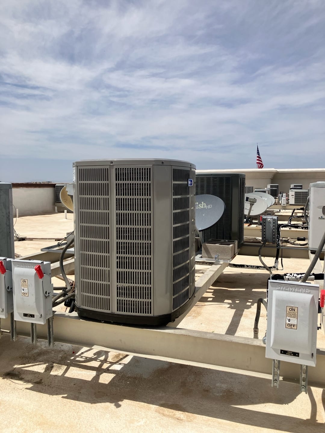 Outdoor heat pump condenser set on a rooftop support frame with adjacent electrical disconnects and insulated refrigerant line set.
