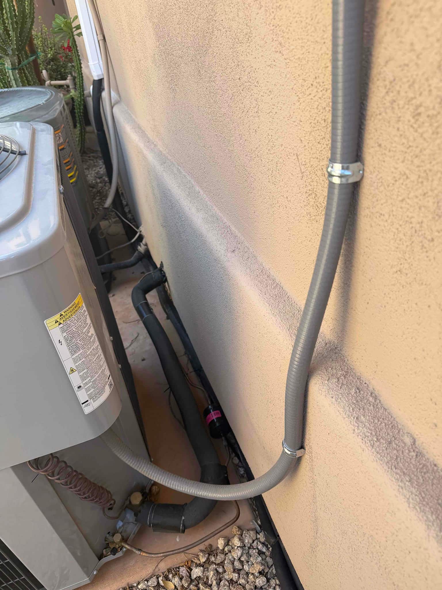 Outdoor mini-split condenser set with insulated refrigerant lines, secured electrical whip, and sealed wall penetration along the exterior wall.