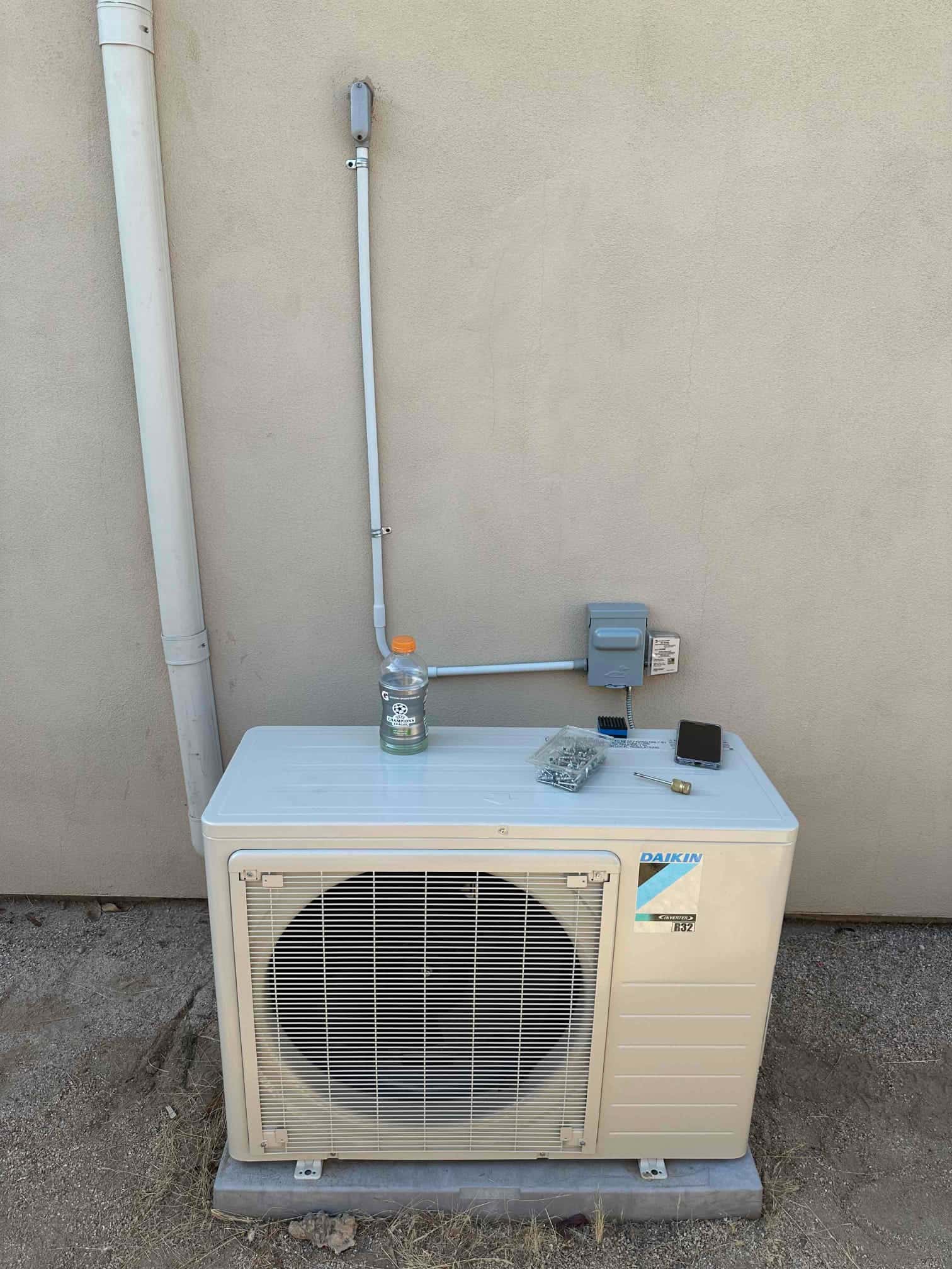 Outdoor mini-split condenser set on a level pad with electrical disconnect and conduit installed on the wall.