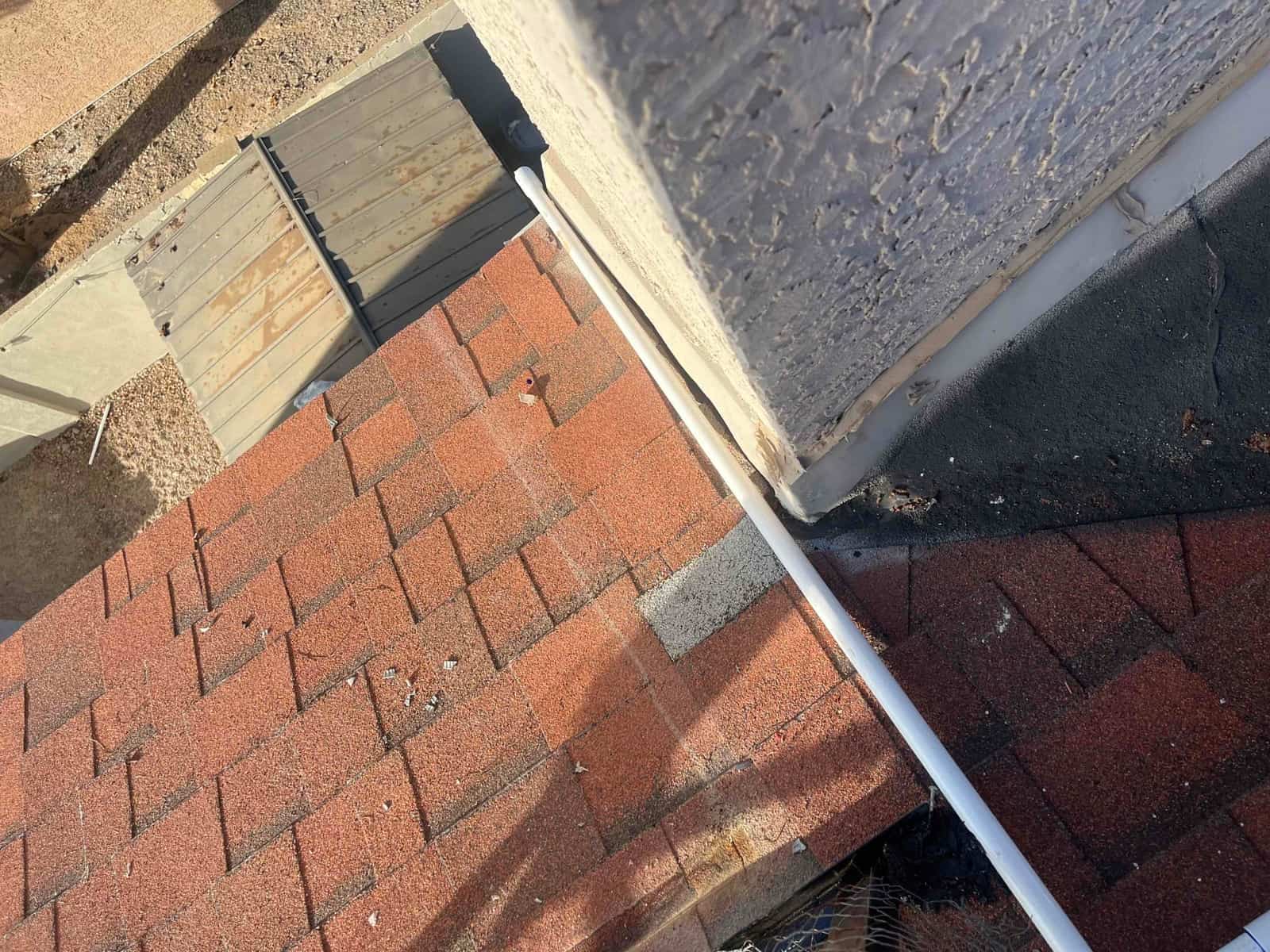 PVC condensate or line-set cover runs along roof edge beside shingles and wall flashing at the installation site.