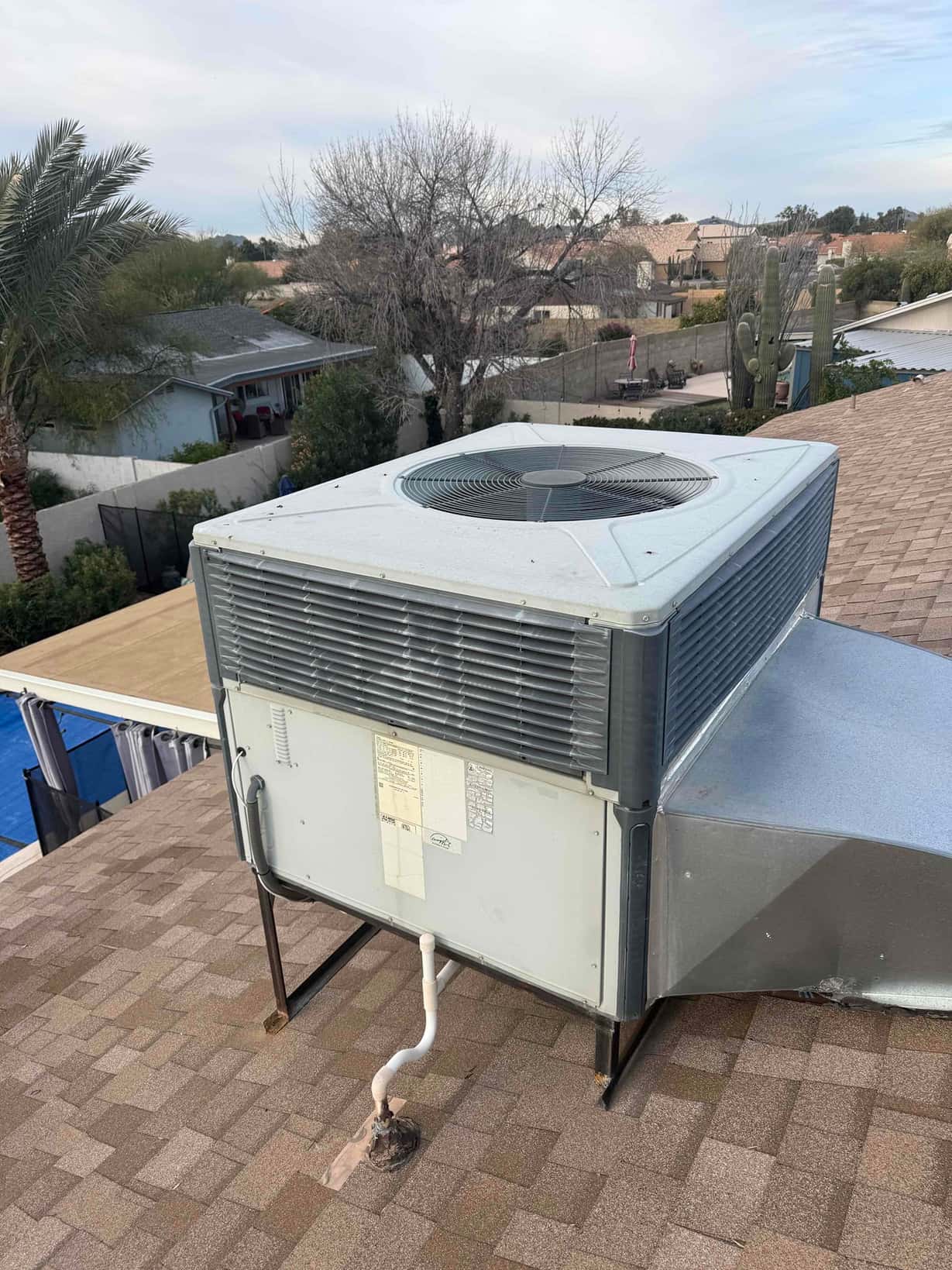 Rooftop packaged air conditioning unit on curb, showing condenser fan grille, cabinet panels, and connected refrigerant line.