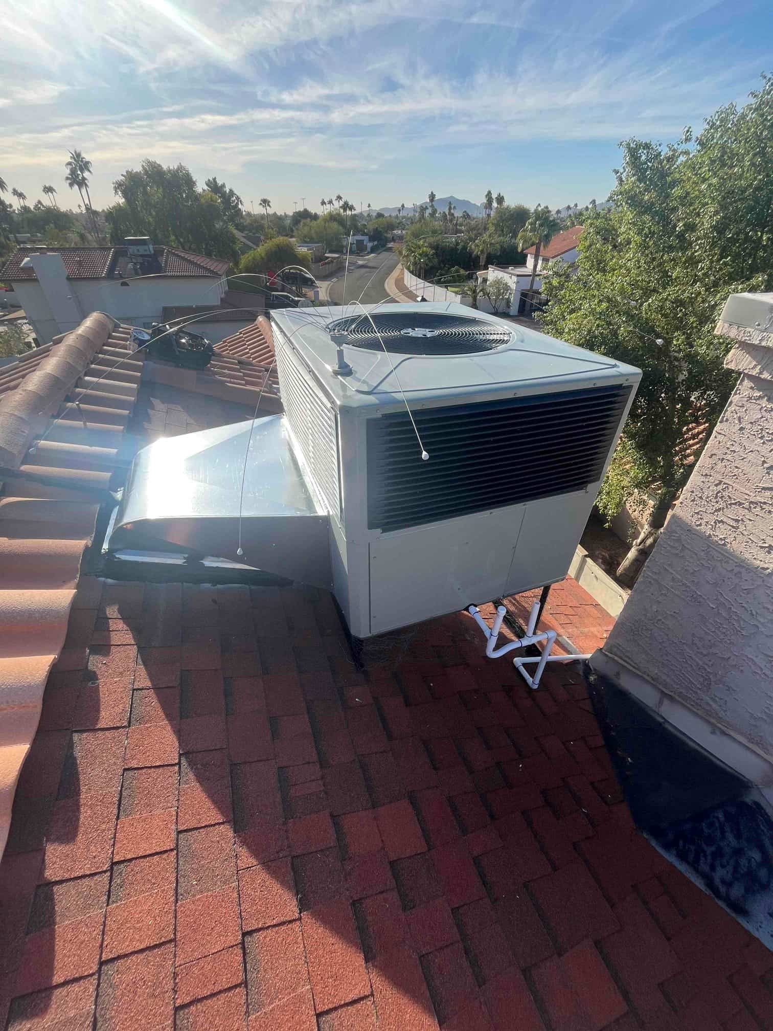 Rooftop packaged HVAC unit freshly installed on curb with sealed flashing and condensate drain piping routed across the shingles.