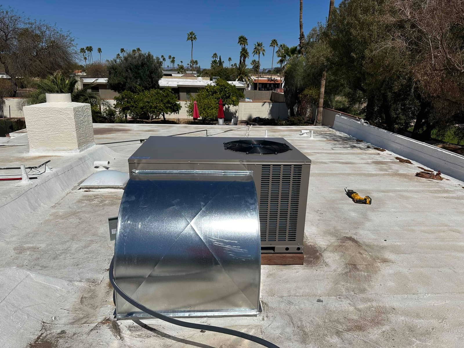 Rooftop packaged HVAC unit newly installed with galvanized supply/return duct transition and sealed roof curb visible.
