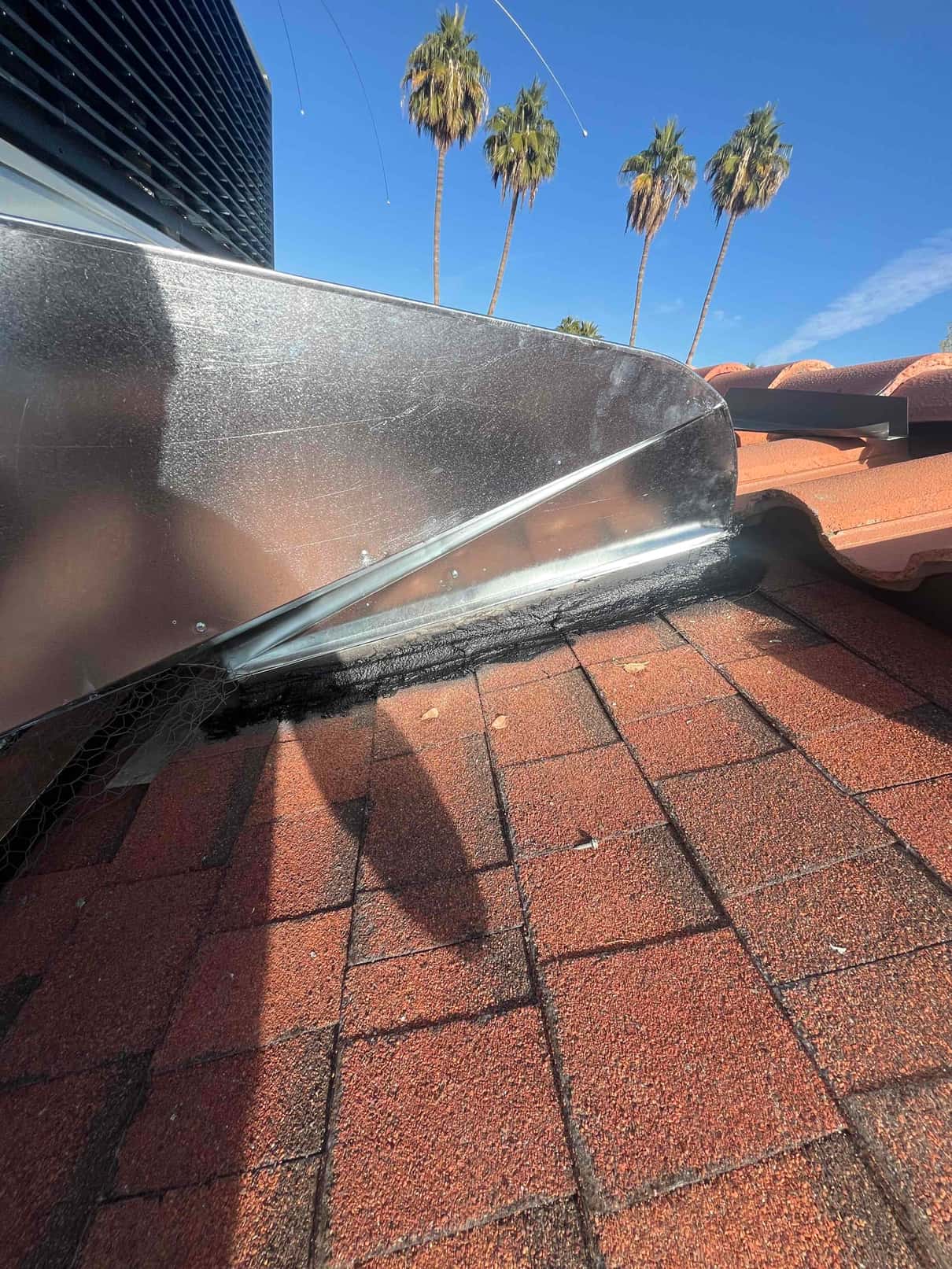 Sheet-metal duct transition on a tiled roof with sealed flashing and mesh, adjacent to the outdoor HVAC unit.