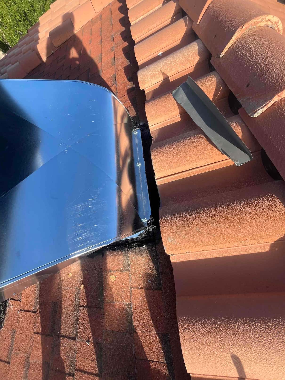 Sheet-metal roof curb or flashing installed against clay tile roofing, sealed at the transition over asphalt shingles.