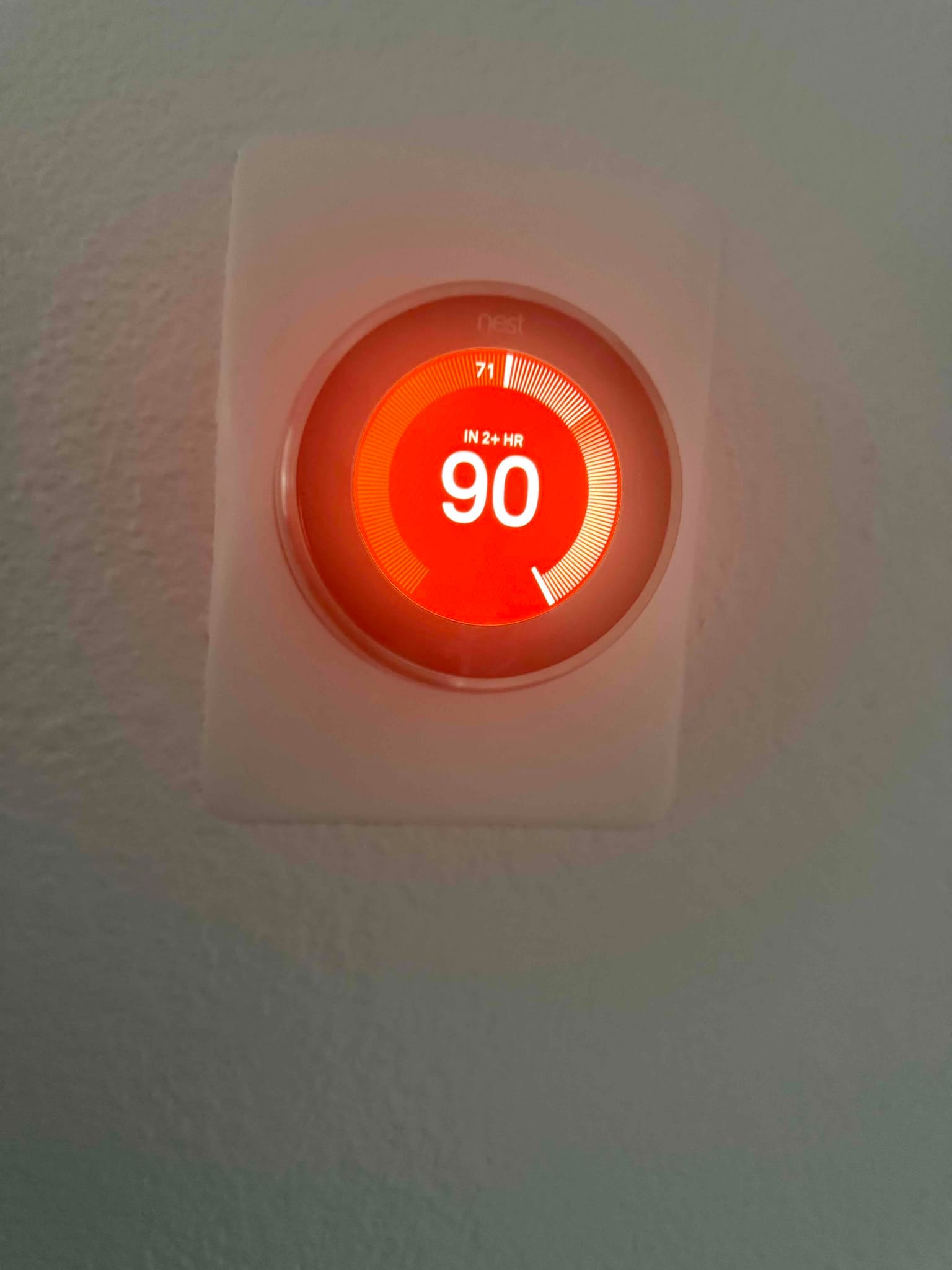 Smart thermostat mounted on an interior wall displaying a heating setpoint with illuminated circular interface.