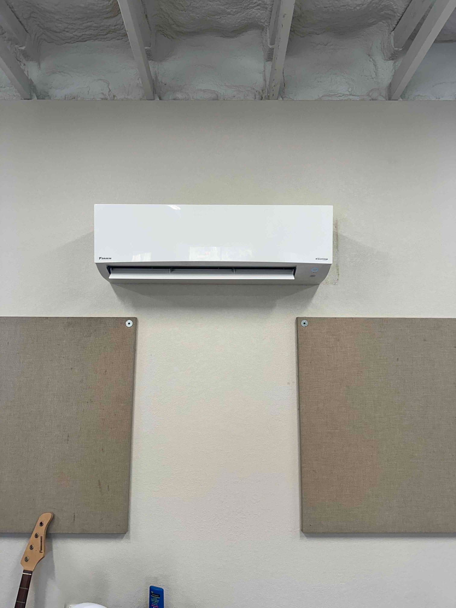 Wall-mounted mini-split indoor unit installed level on a finished wall beneath a sprayed-foam ceiling in a clean space.