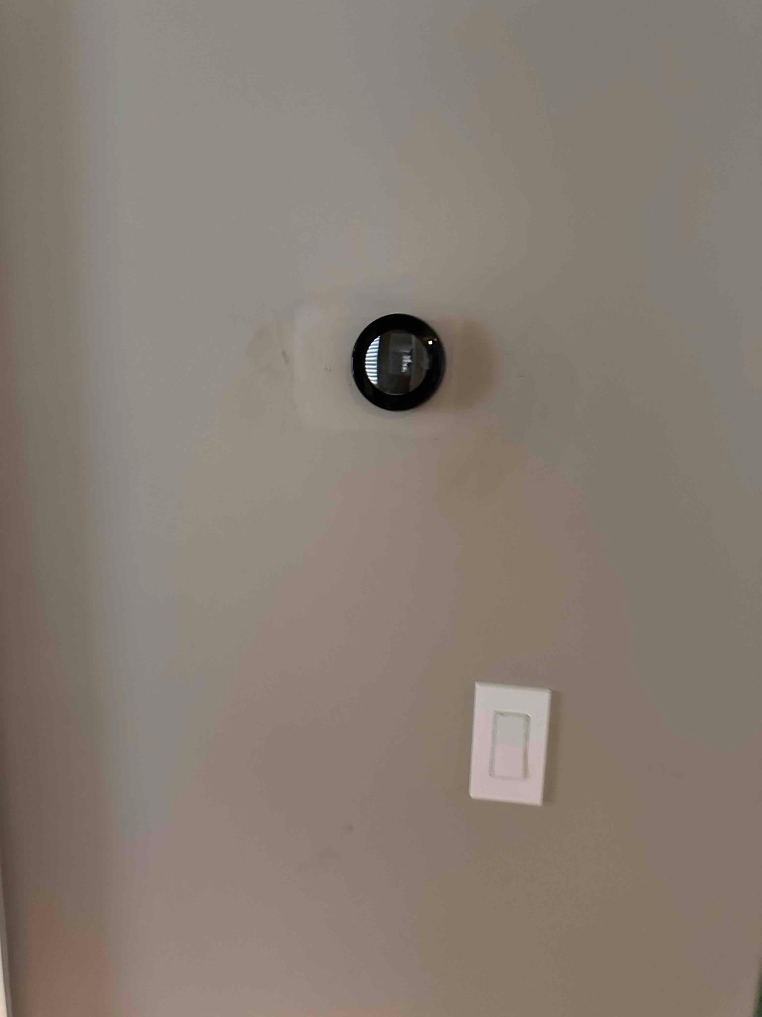 Wall-mounted smart thermostat installed above a light switch on a finished interior wall during HVAC retrofit.