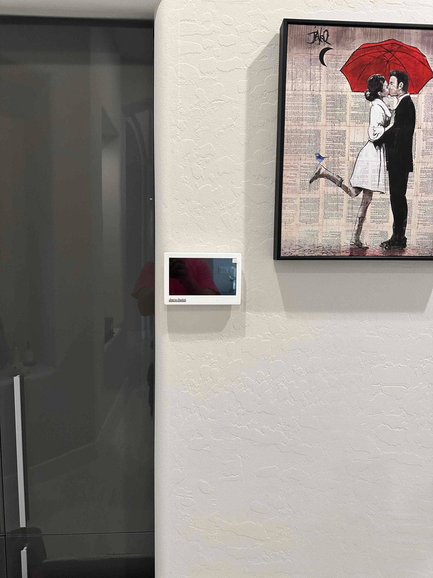 Wall-mounted smart thermostat installed neatly in the hallway, adjacent to a framed artwork and glass door.