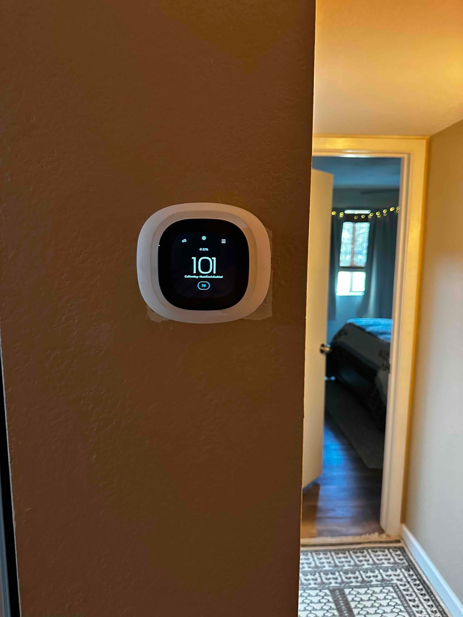 Wall-mounted smart thermostat installed and powered on, displaying a setup countdown on the screen in a hallway.