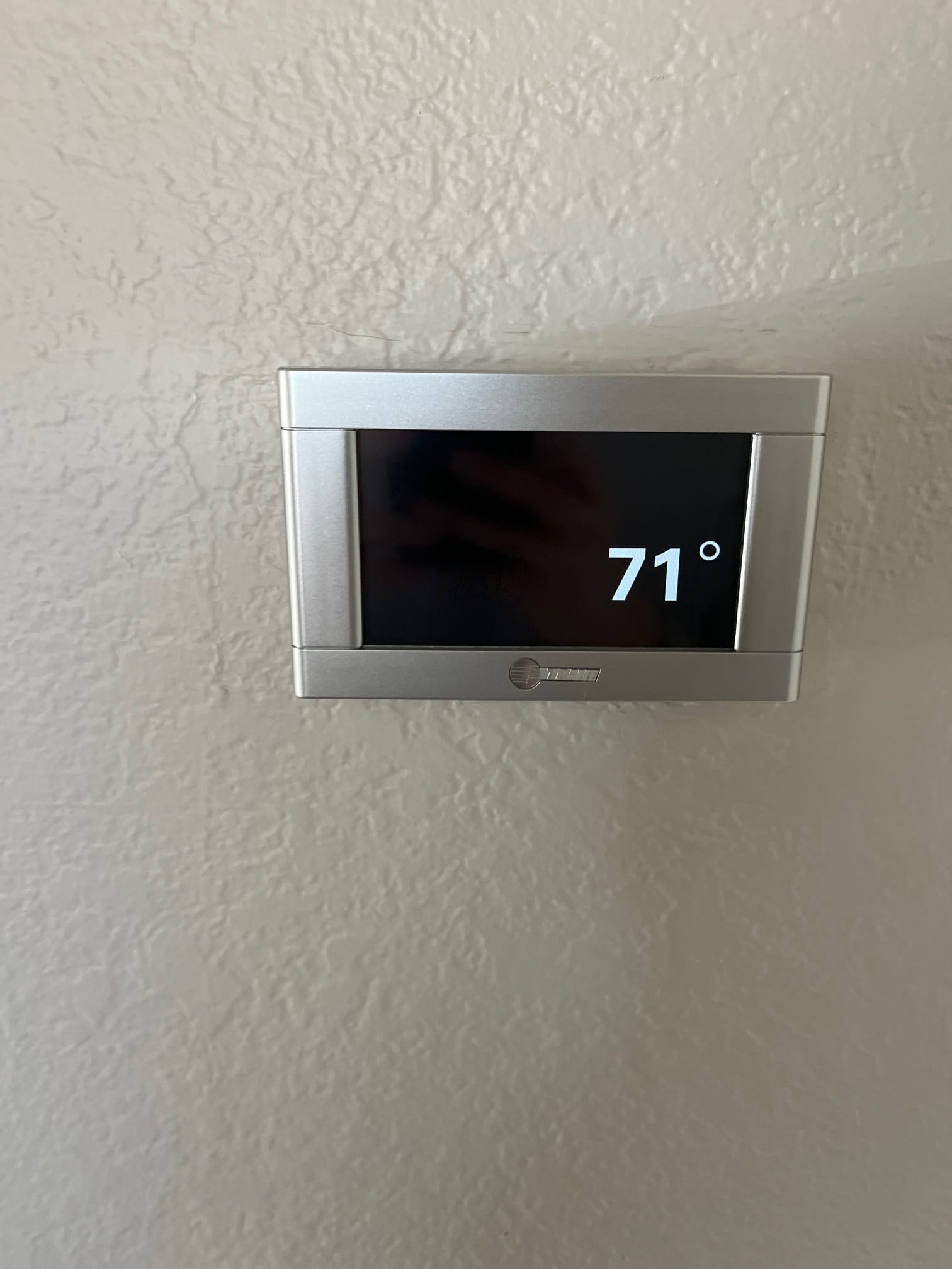 Wall-mounted thermostat displays 71 degrees, confirming control installation and system interface after HVAC setup.
