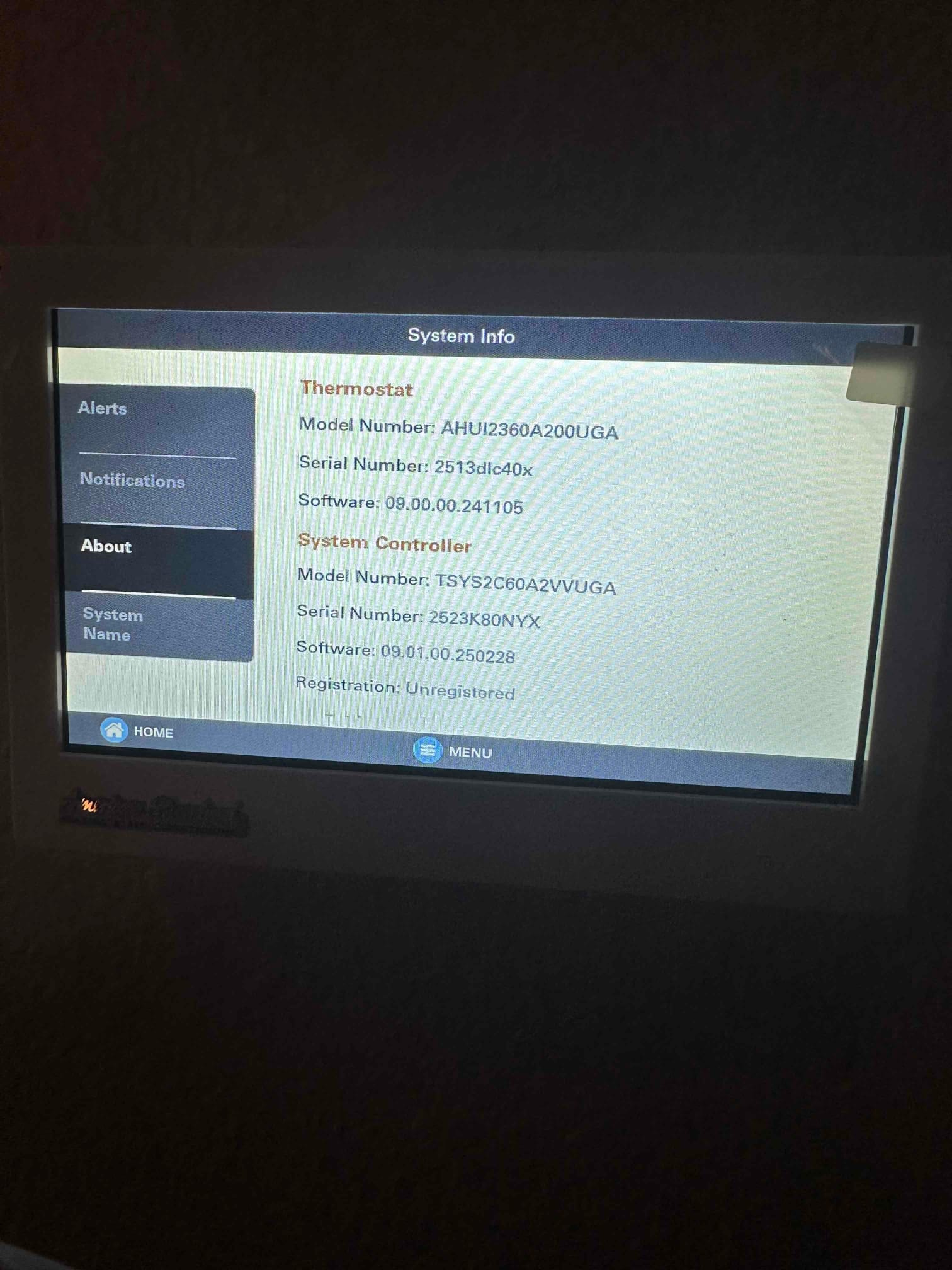 Wall-mounted touchscreen thermostat displays system information menu after installation, showing thermostat and system controller details on screen.